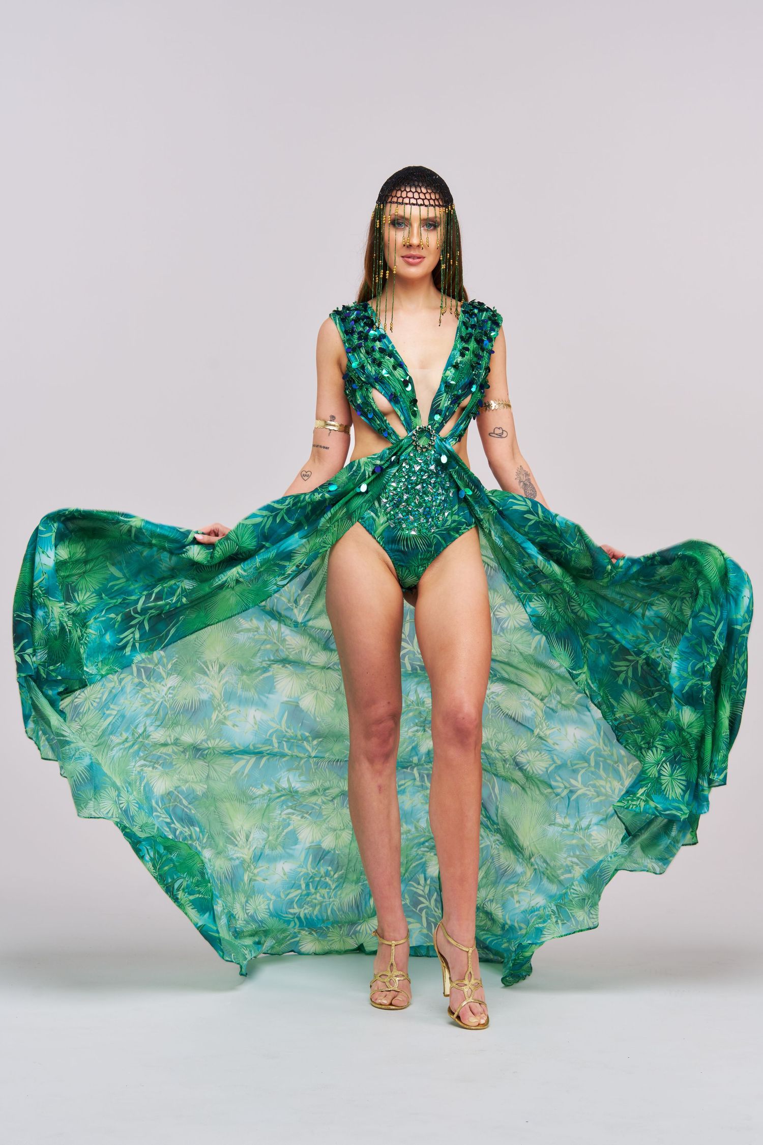 Model poses in emerald green bodysuit with flowing sheer cape in dynamic fashion photography sequence.
