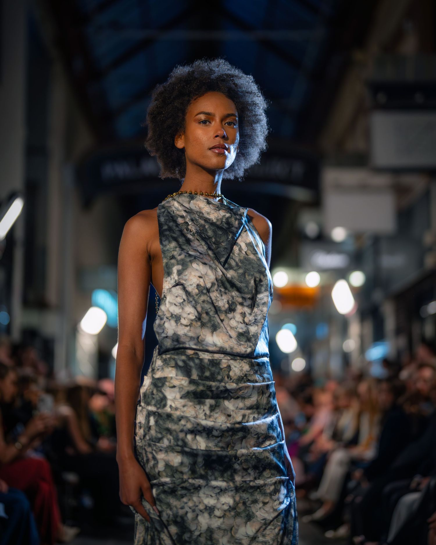 A model walks down a runway wearing a sleeveless camouflage print dress during a fashion show.
