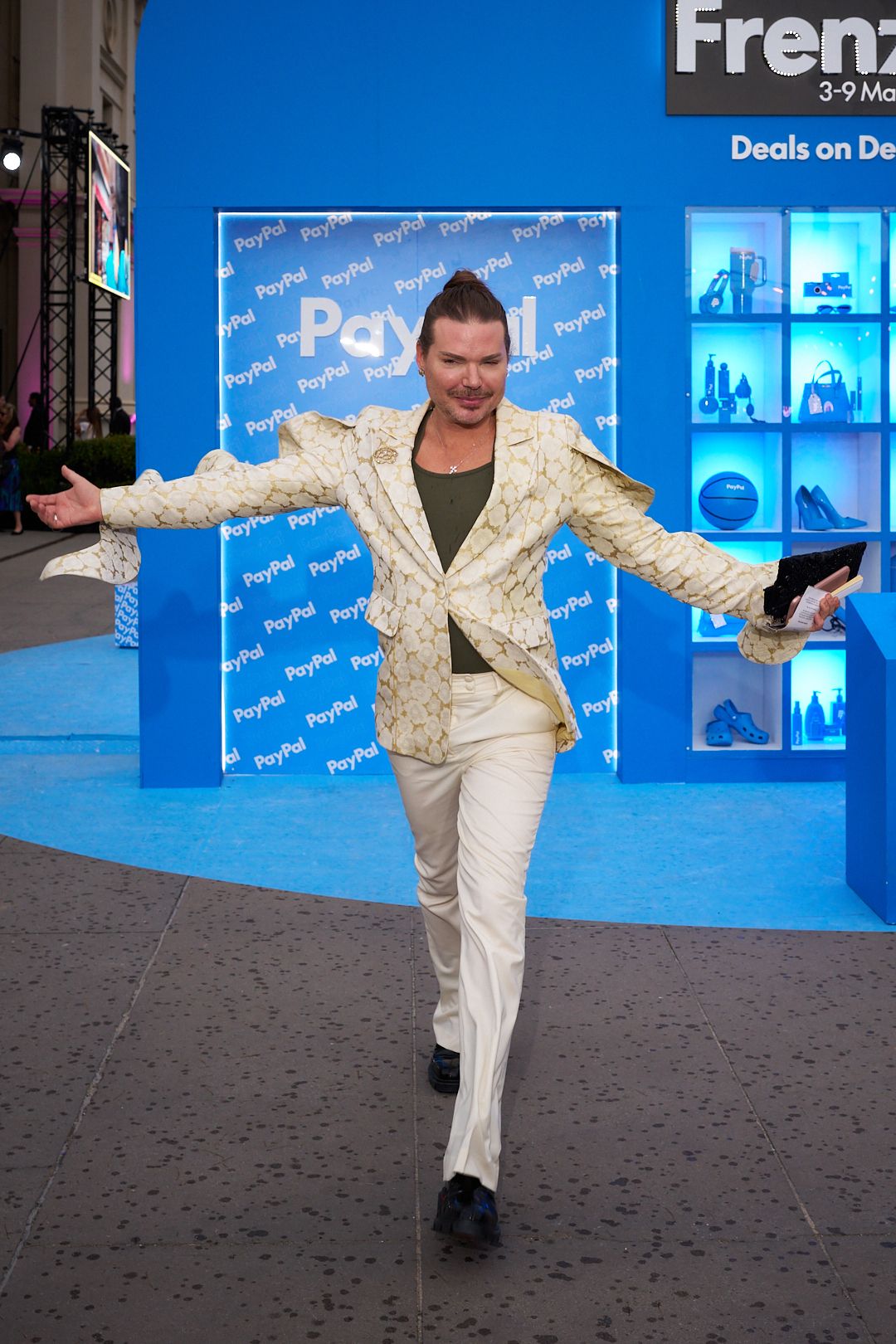 Person in a white sequined suit performs energetic dance moves on a blue carpet at an event.