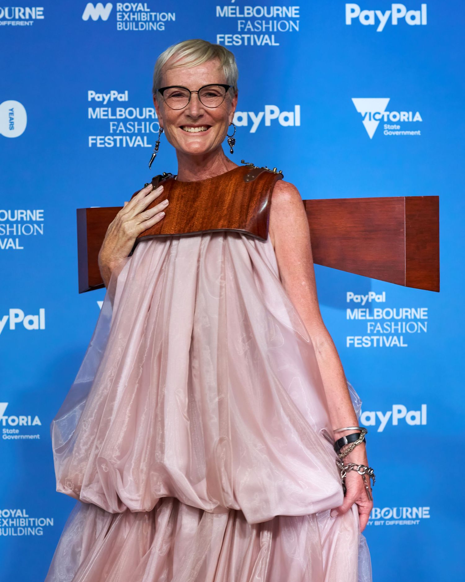 Person in pink bubble dress and brown accent piece poses at PayPal Melbourne Fashion Festival event with branded backdrop.