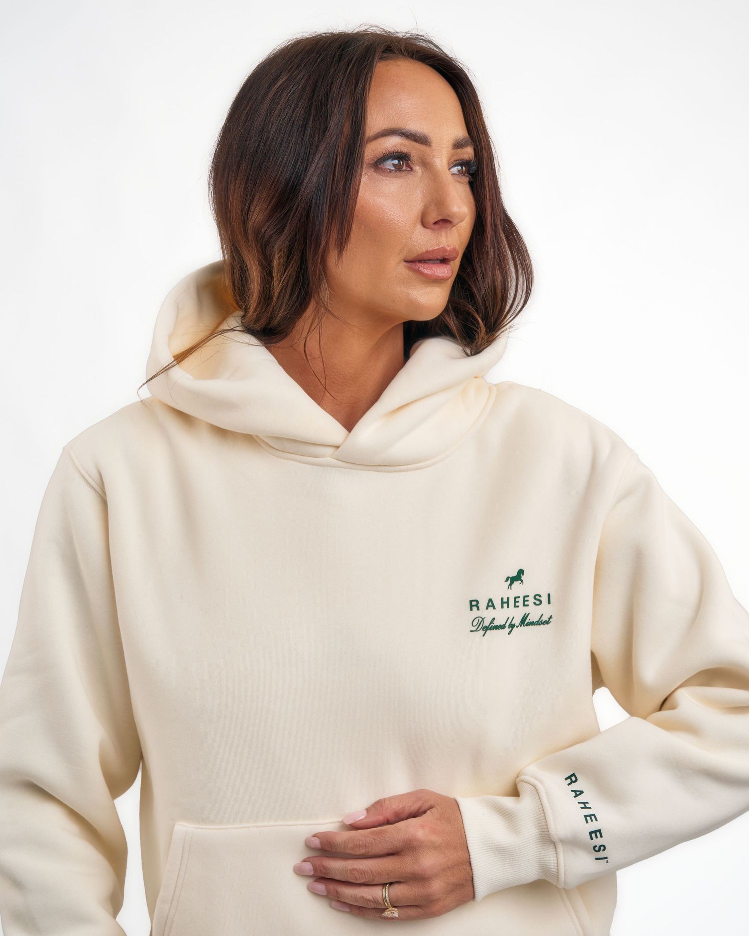Close-up of woman in cream oversized hoodie with green Raheesi embroidered logo on chest and sleeve.