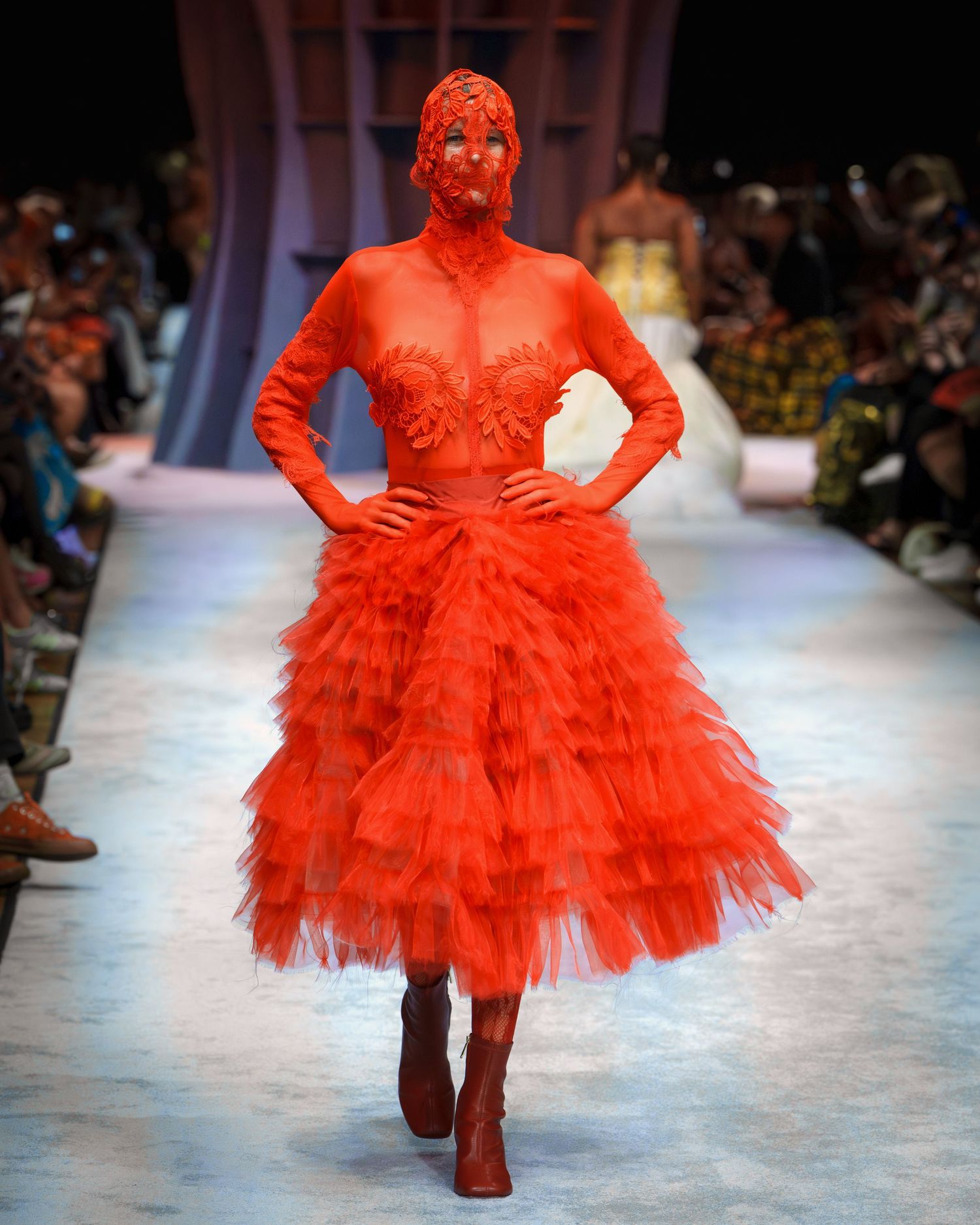A dramatic bright red tulle gown with matching bodysuit and boots showcased on a fashion runway.