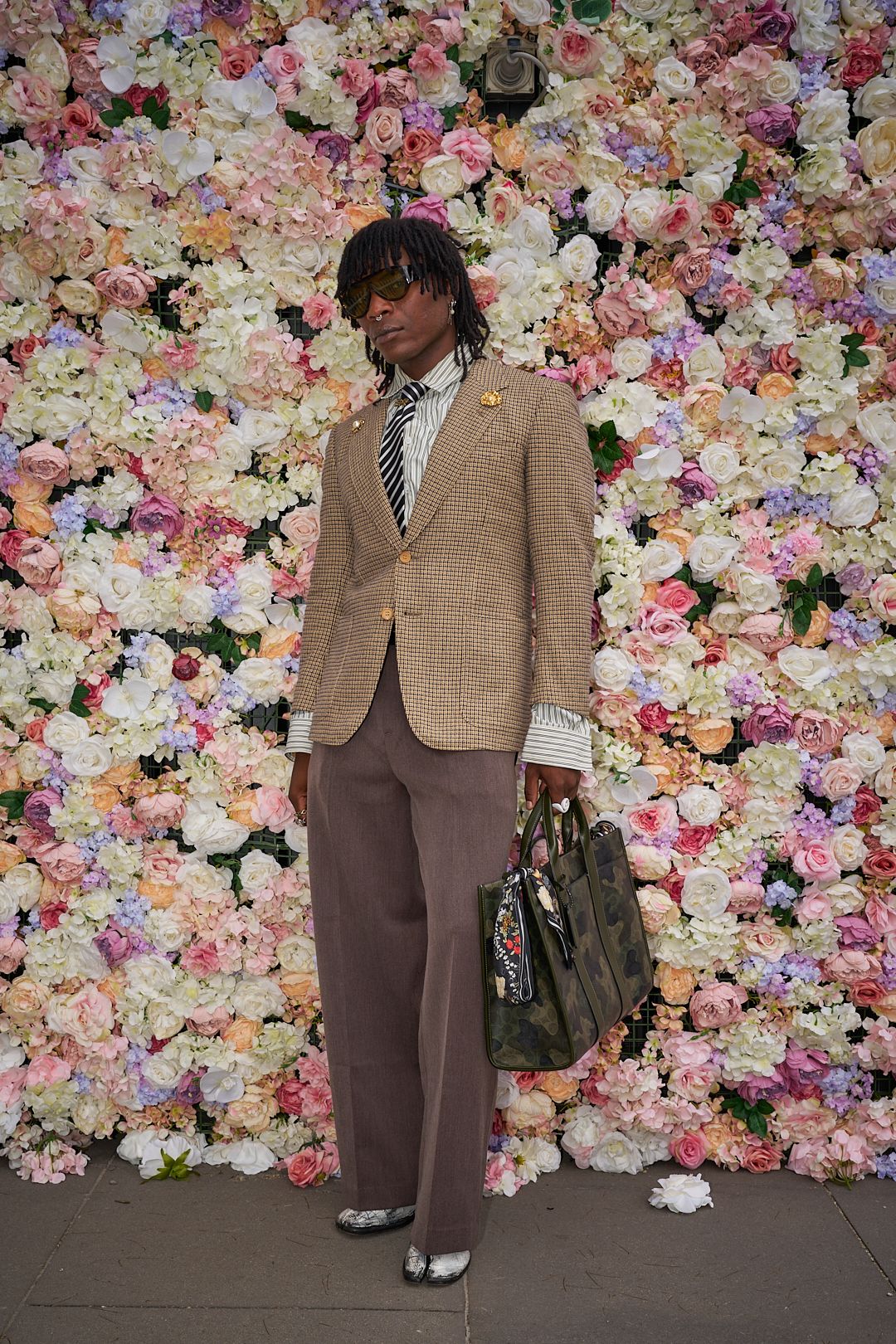Stylish outfit with beige blazer and brown pants against vibrant floral wall backdrop with pink and purple blooms.