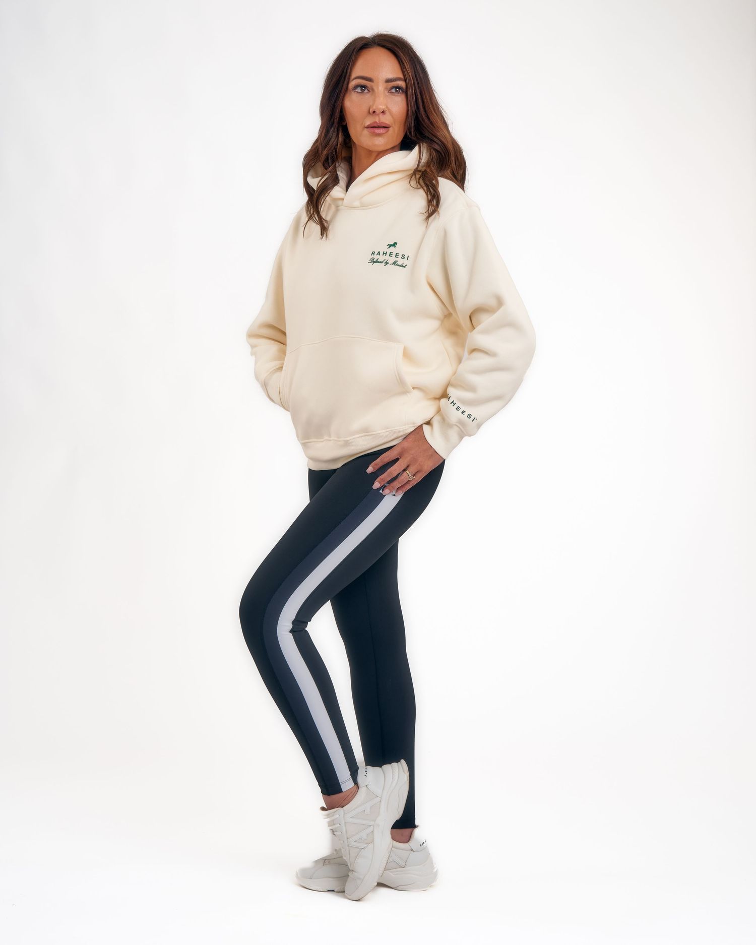 Woman in cream Raheesi hoodie and navy striped leggings with white sneakers.