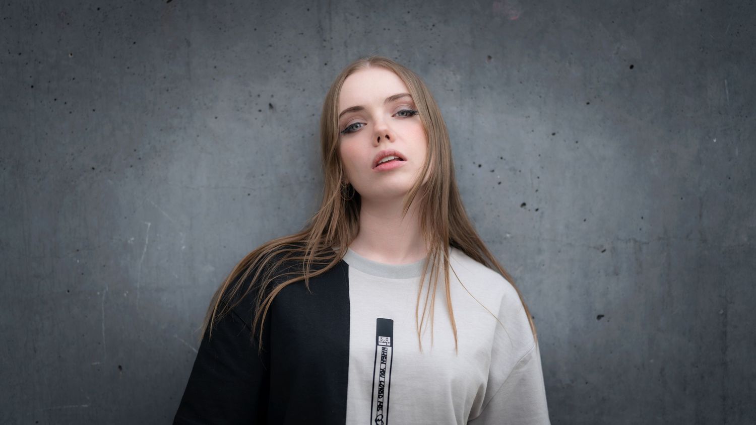 Portrait of young woman in white top against industrial concrete wall with dramatic lighting and composition.