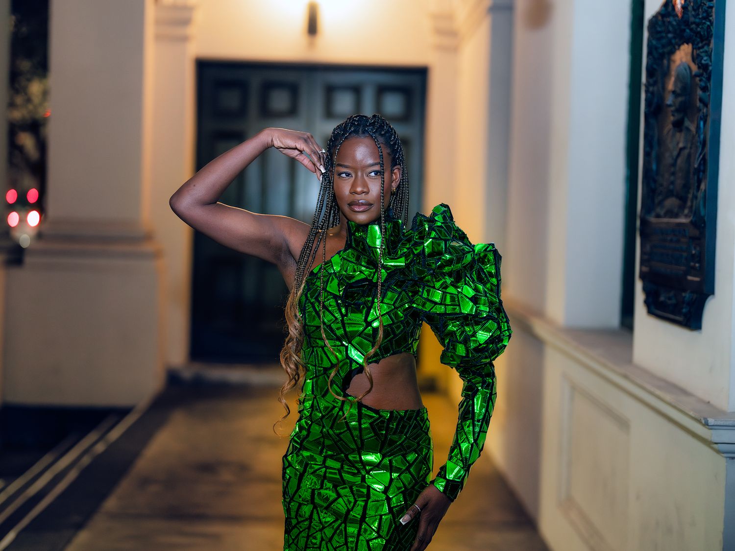 Two people in bright emerald green sparkly outfits dance together in an elegant hallway.