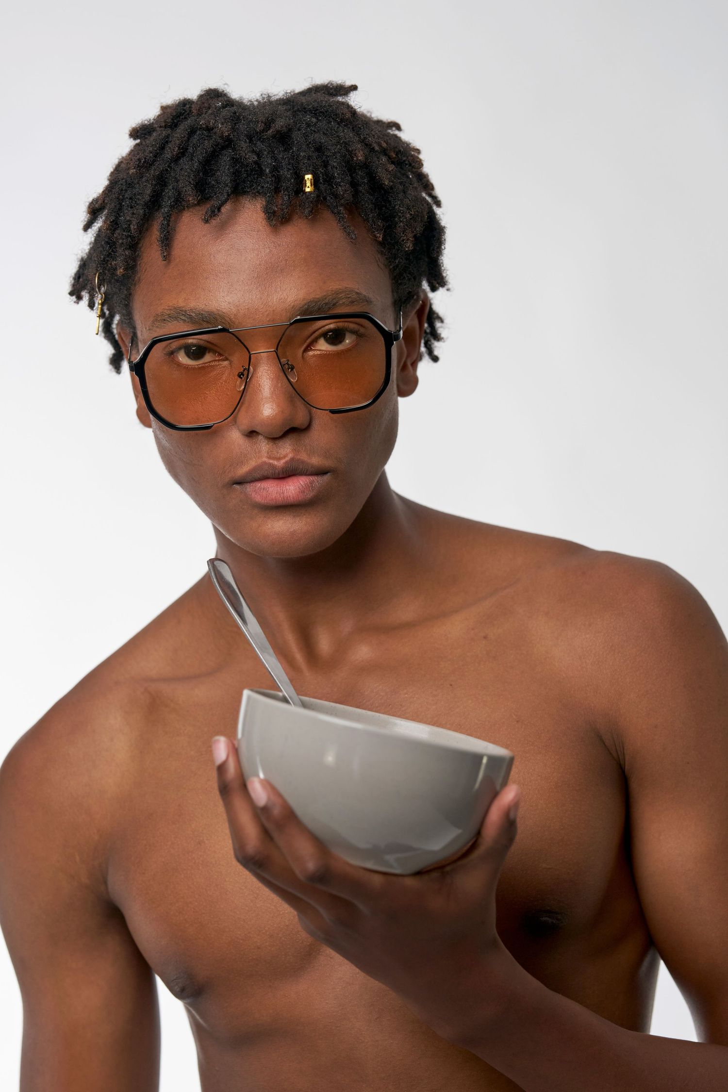 A person wearing brown glasses holds a gray ceramic bowl against a white background.