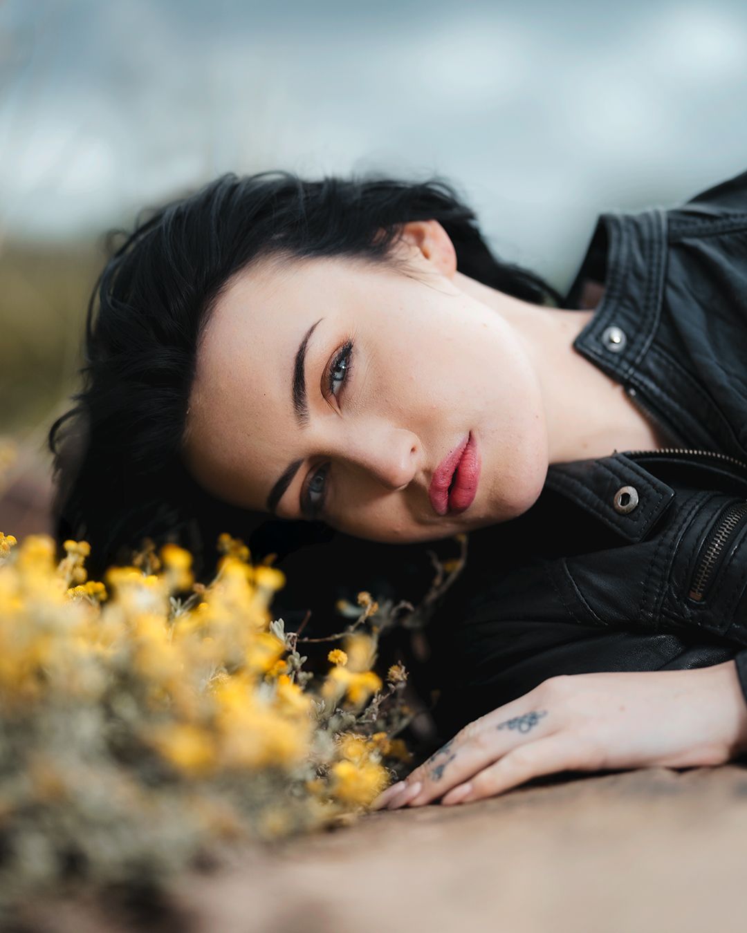 Artistic portrait with black leather jacket amid yellow wildflowers in soft natural lighting.
