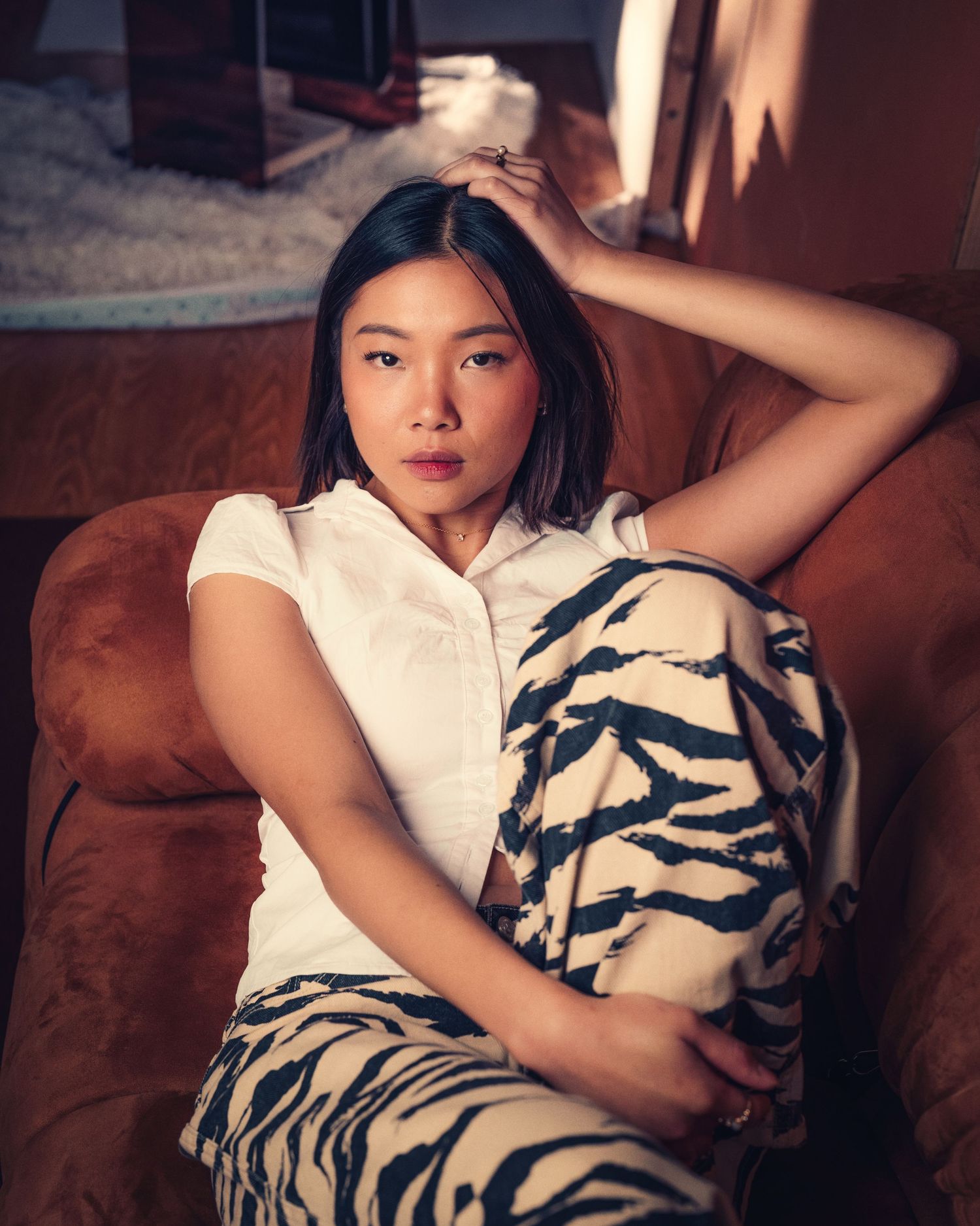Fashion portrait of someone lounging on brown couch in white top and patterned pants.