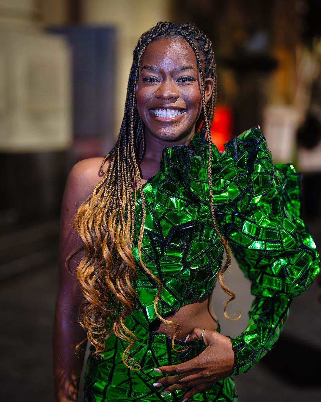 Person in black sequin dress holding shimmering green decoration with radiant smile.