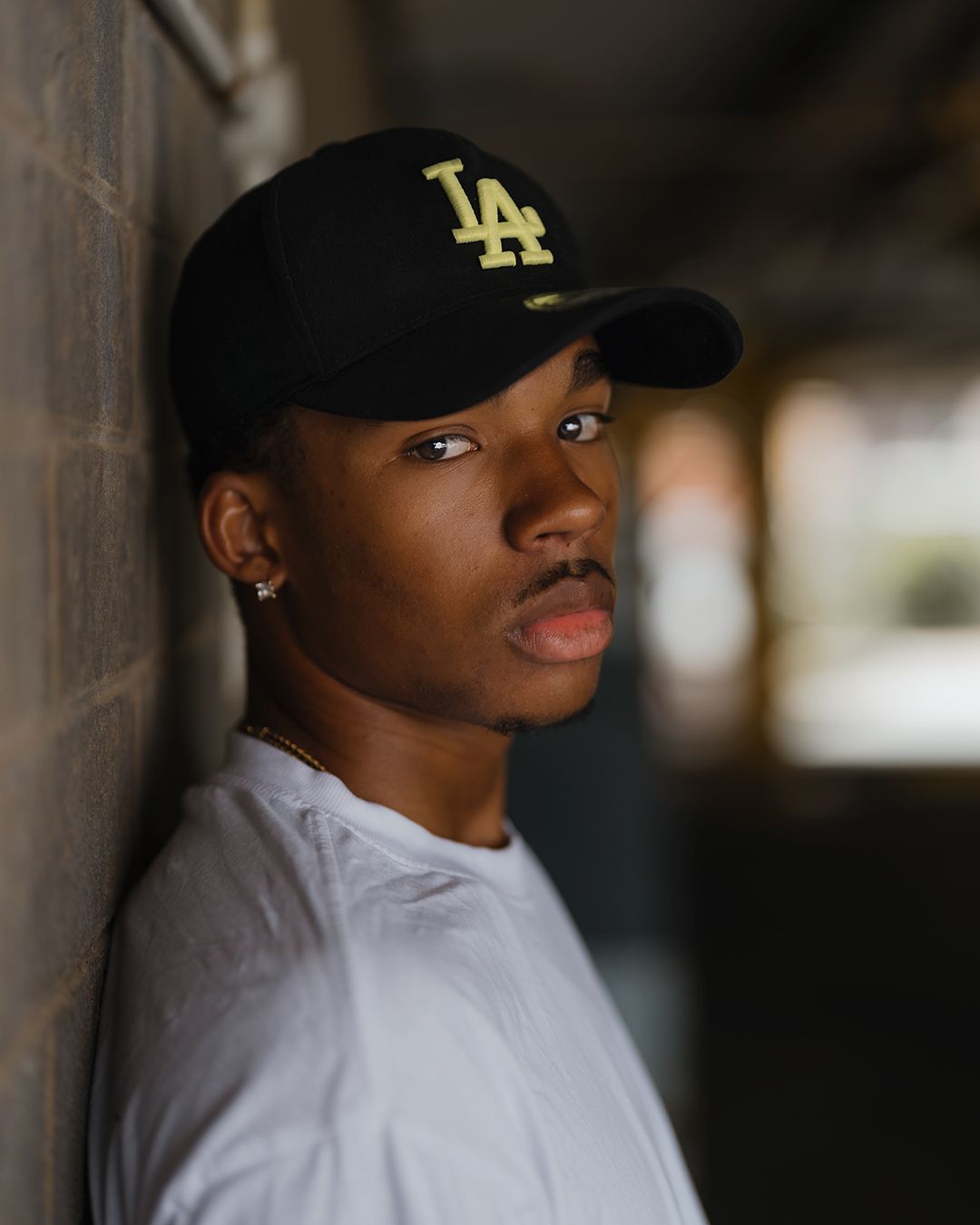 Dramatic portrait against wall wearing LA Dodgers baseball cap and white t-shirt.