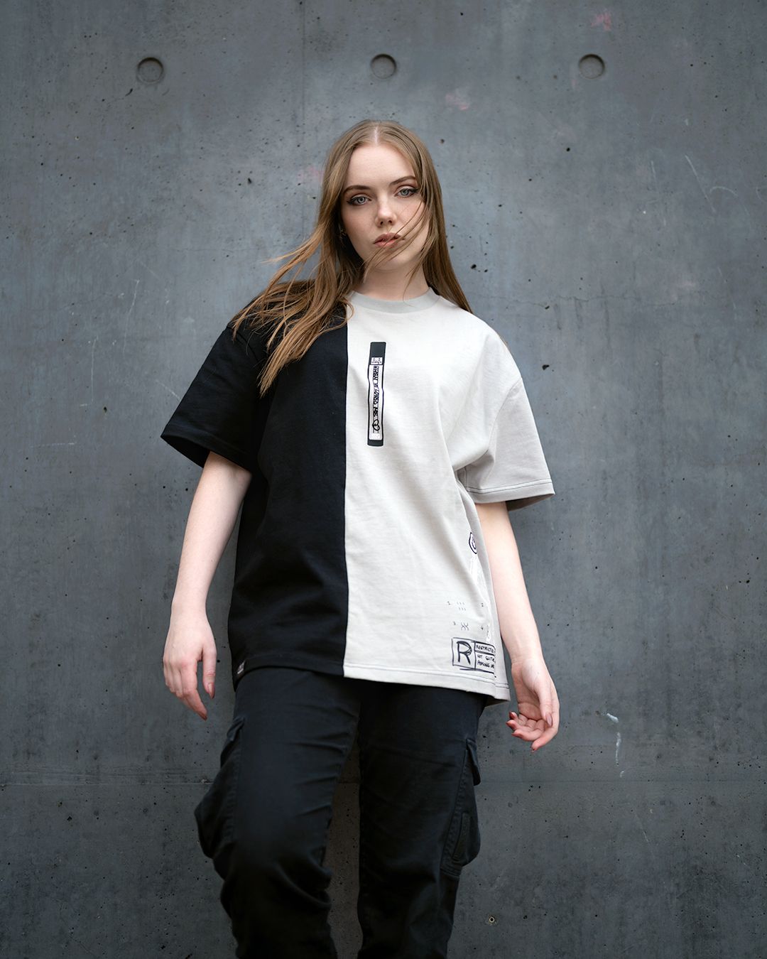 Streetwear fashion shot featuring split-design t-shirt and cargo pants against concrete backdrop.