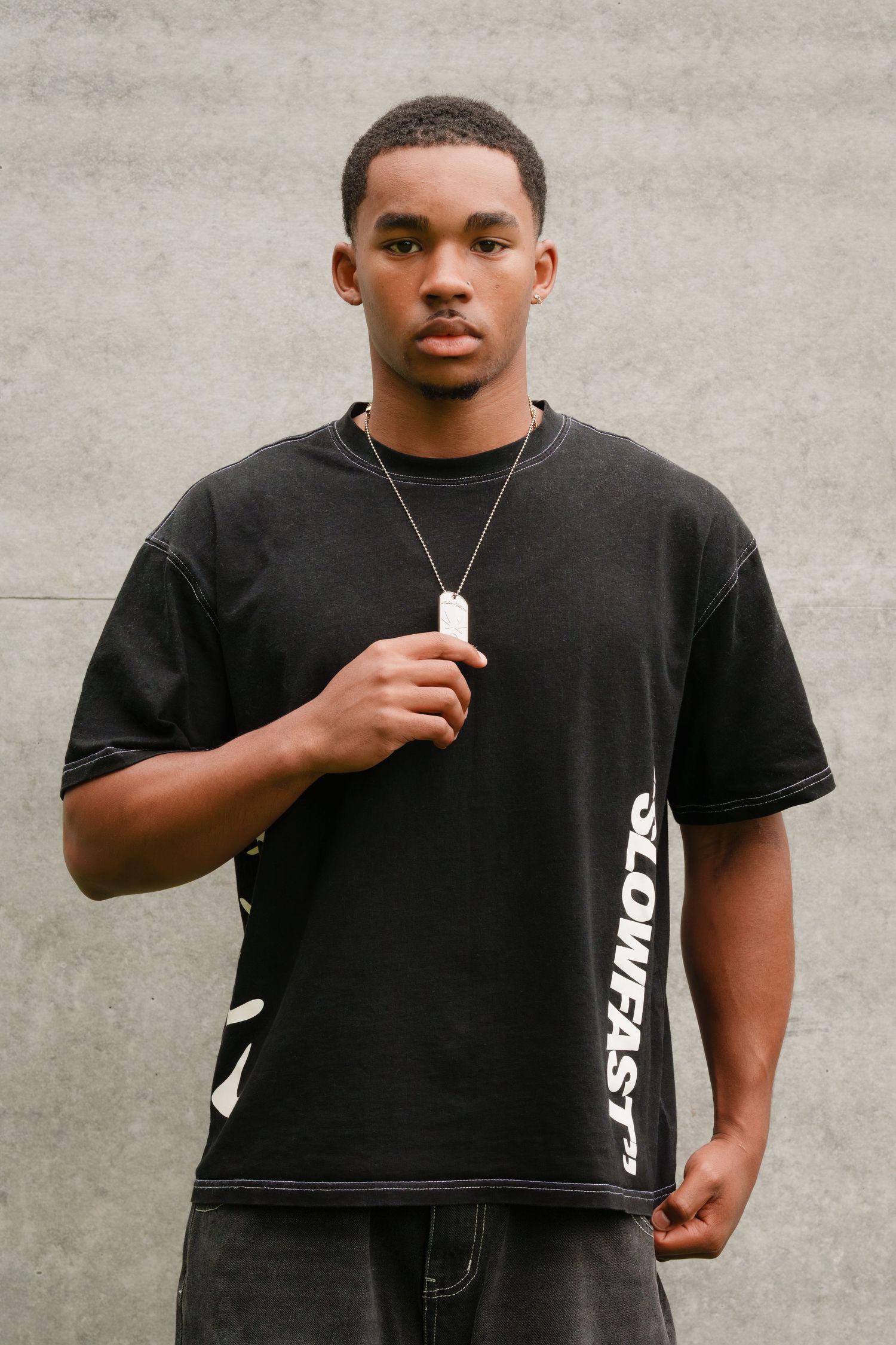 A person in a black t-shirt with white side text stands against a gray wall in multiple poses.