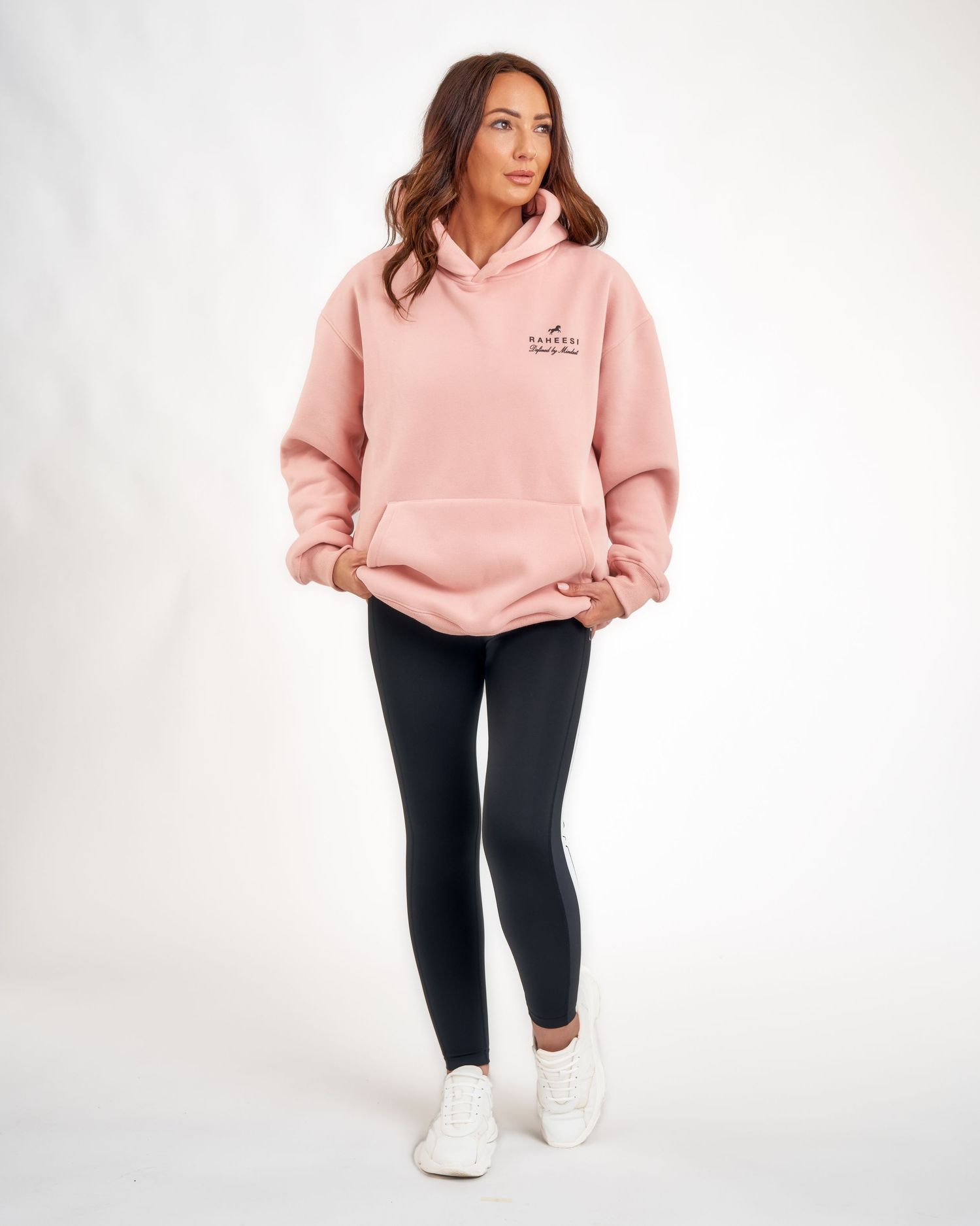 Woman wearing an oversized pink hoodie with black leggings and white sneakers, full-length casual athleisure outfit.
