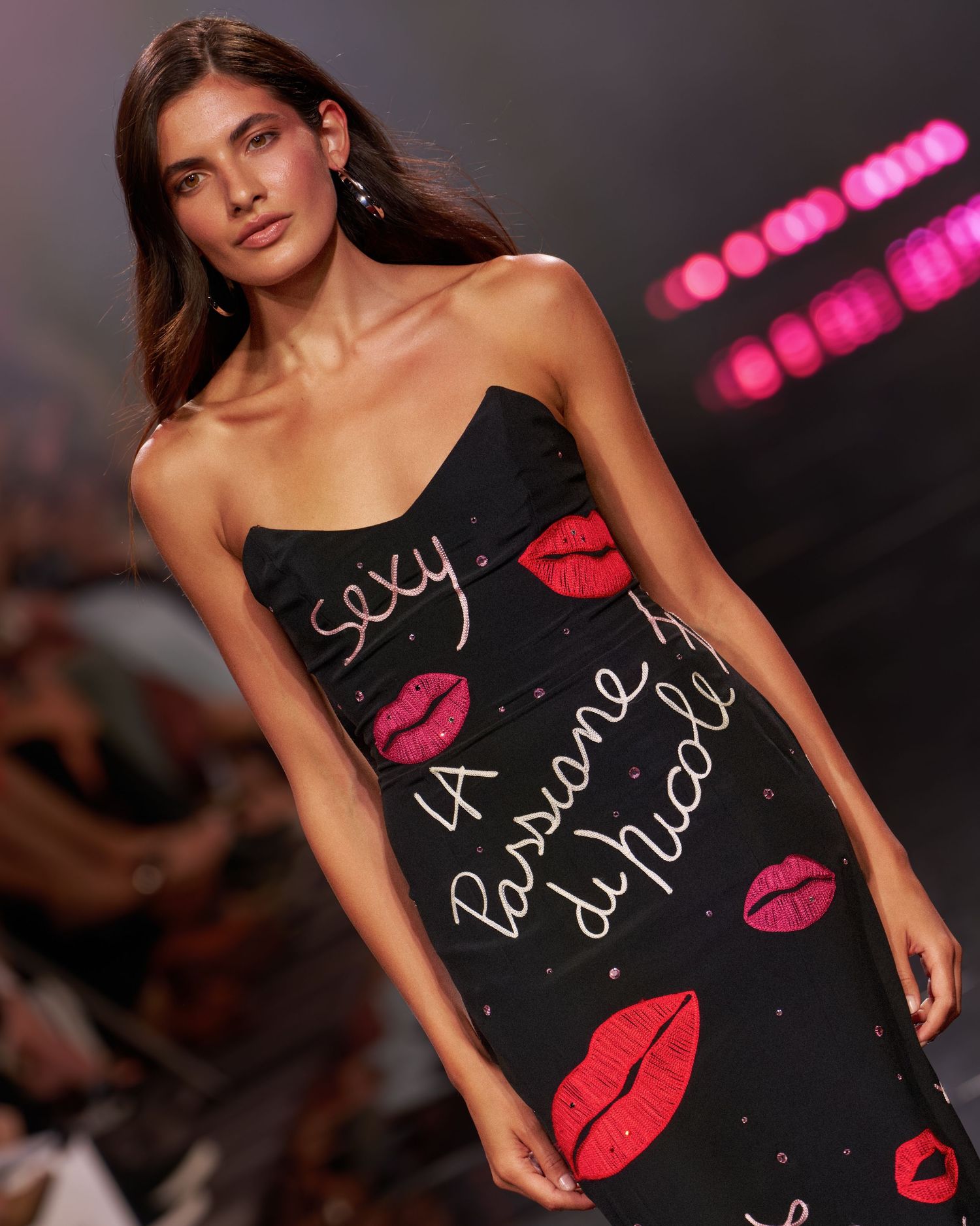 Model walks runway in black strapless dress with red lip prints and cursive text reading sexy, La Passione di Nicole.