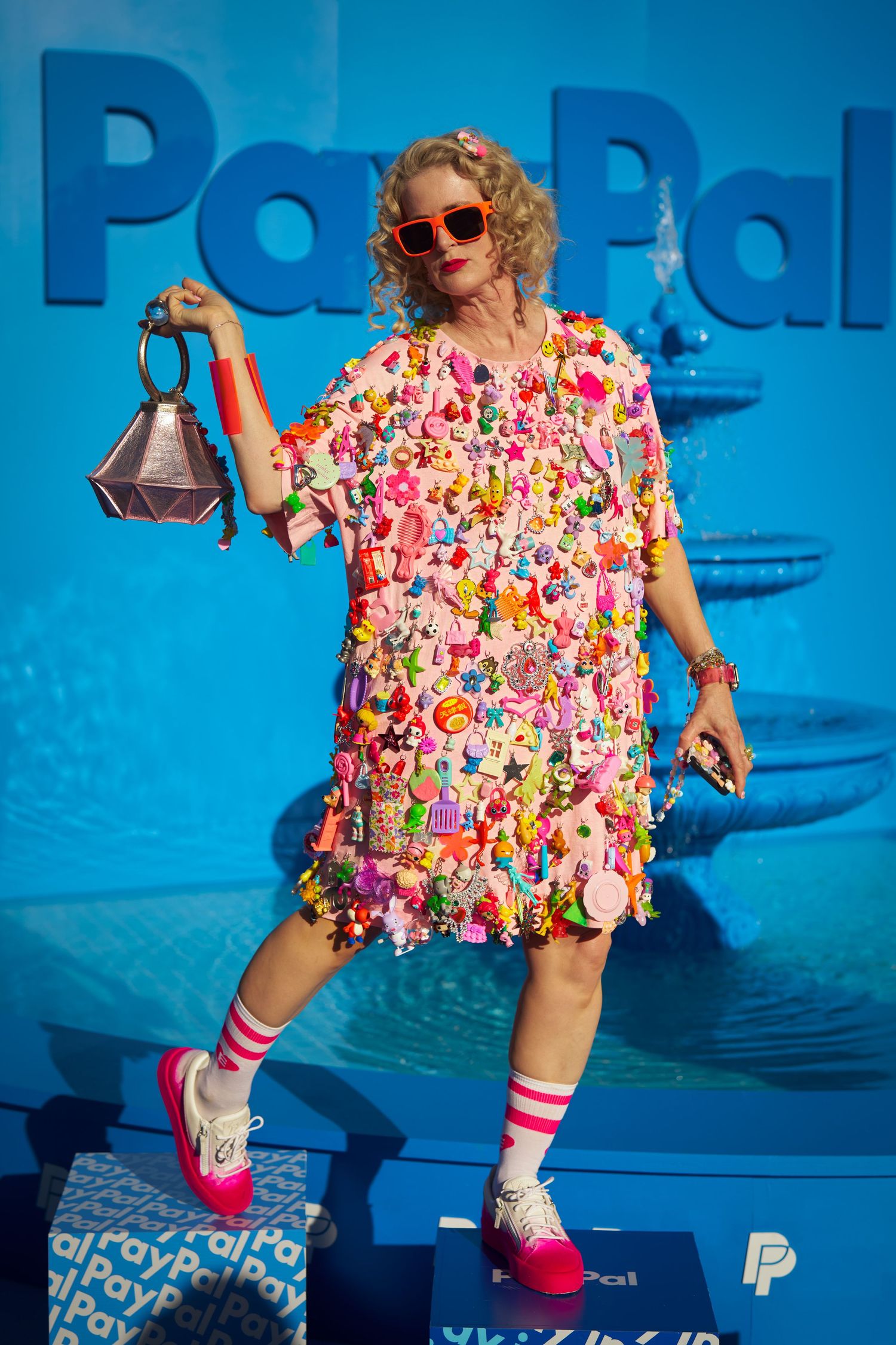 Vibrant fashion photo against blue background featuring colorful floral dress and striped knee socks with playful pose.