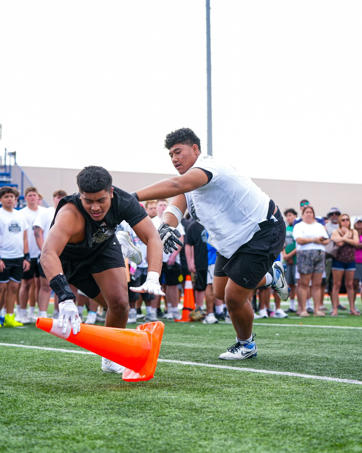 Athletes compete in an agility drill around orange cones on a turf field as spectators watch from the sidelines.