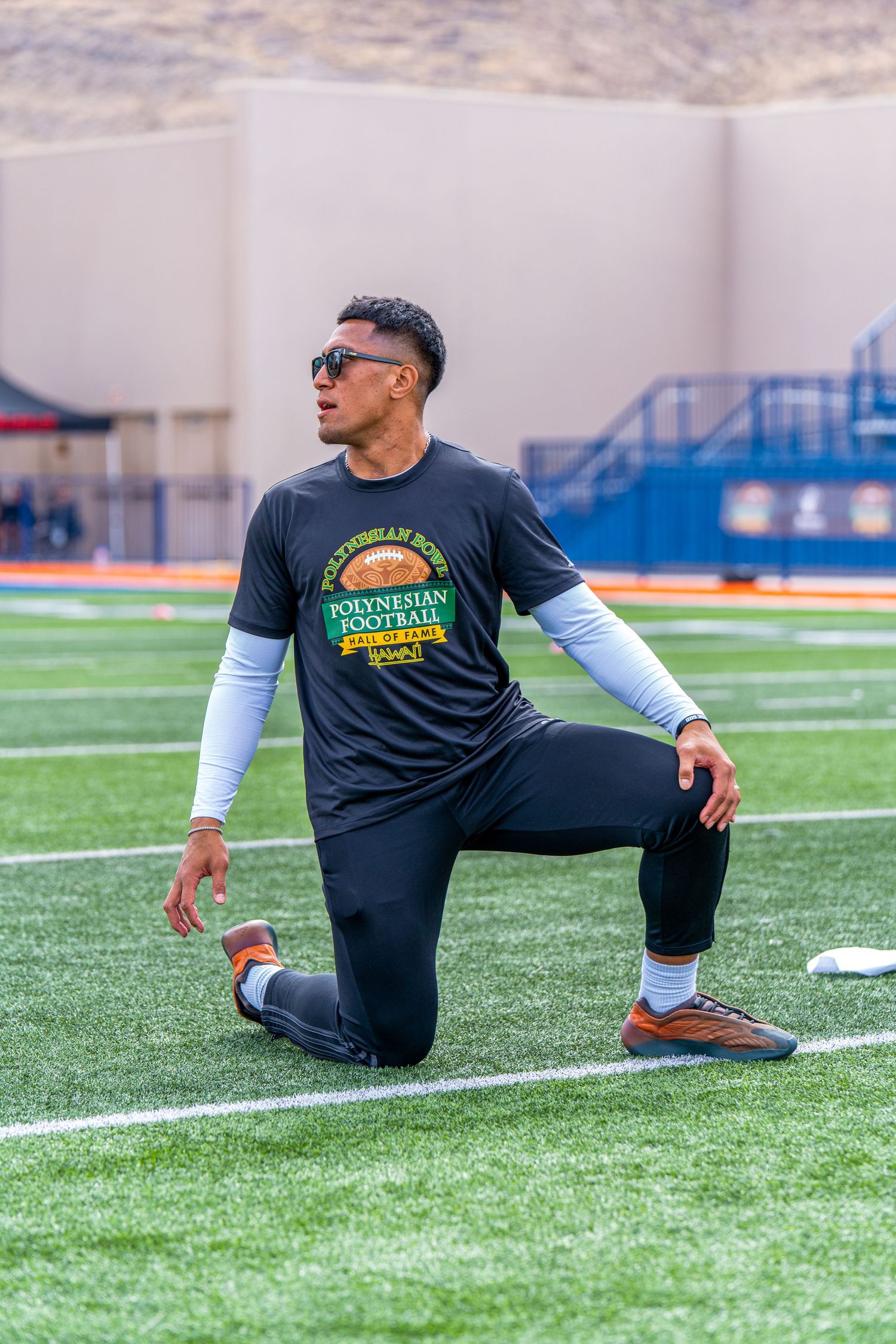 Athlete in sporty attire stretching on football field wearing Polynesian Football branded shirt.