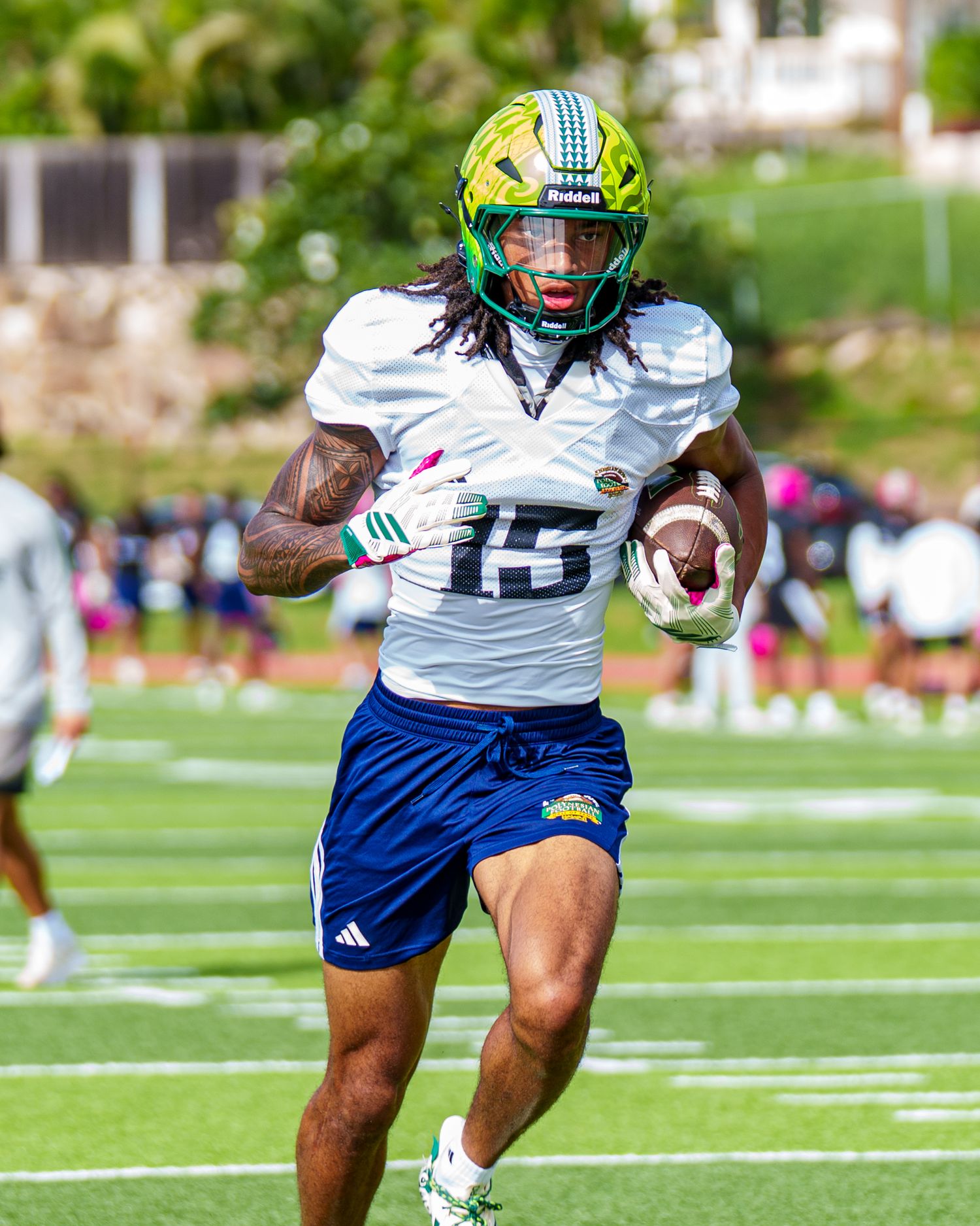 Football player in blue and white uniform runs with ball during practice drill on outdoor field.