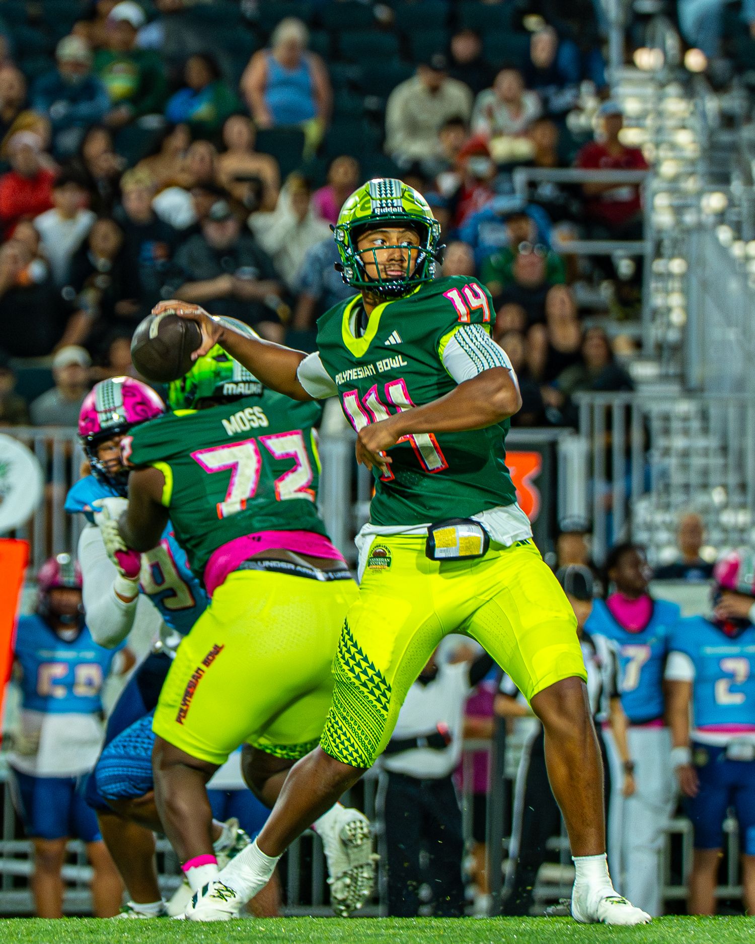 Football player in bright green uniform throws a pass during a game with stadium crowd in background.