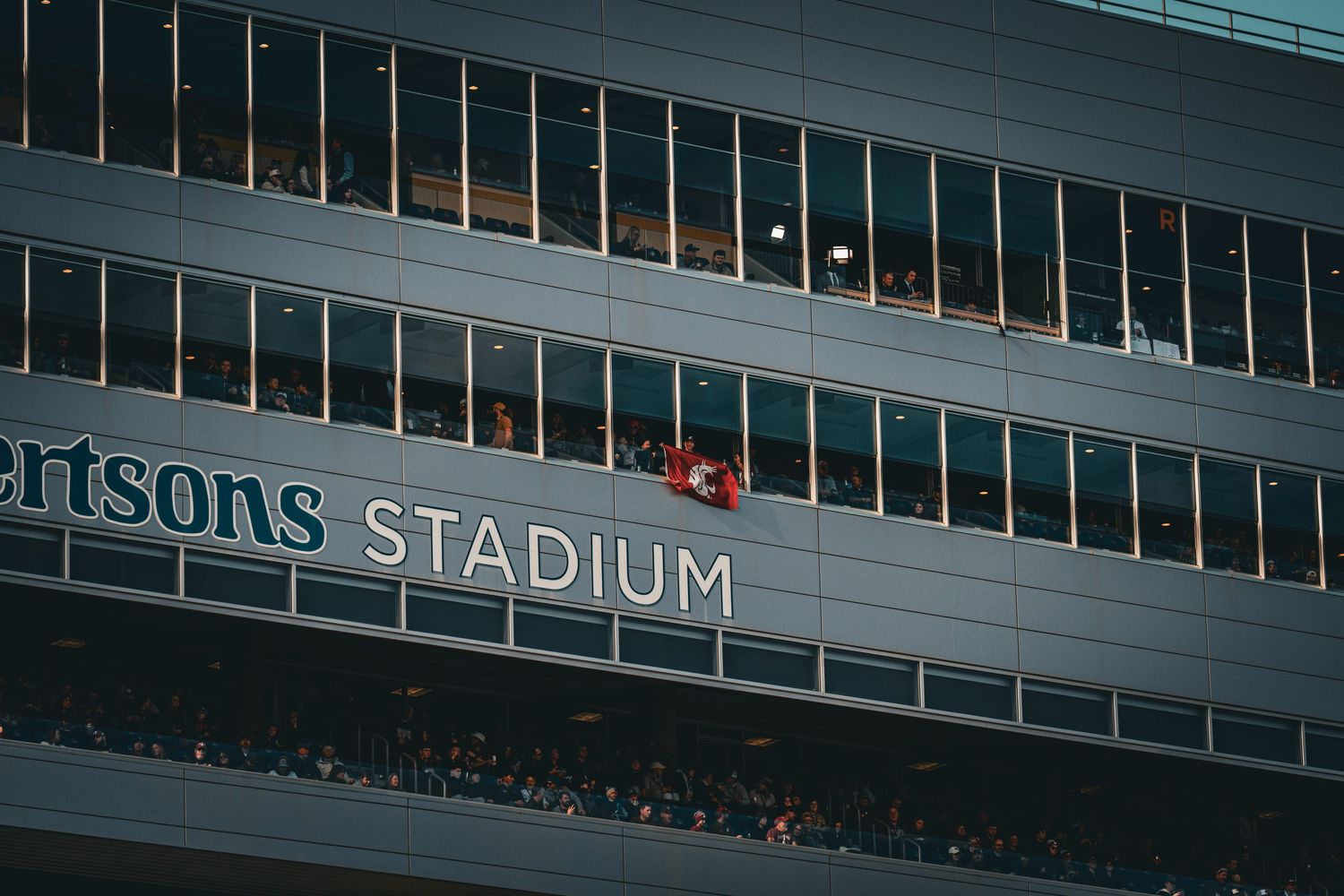 Exterior view of Ericsson Stadium with illuminated windows and signage during evening hours.