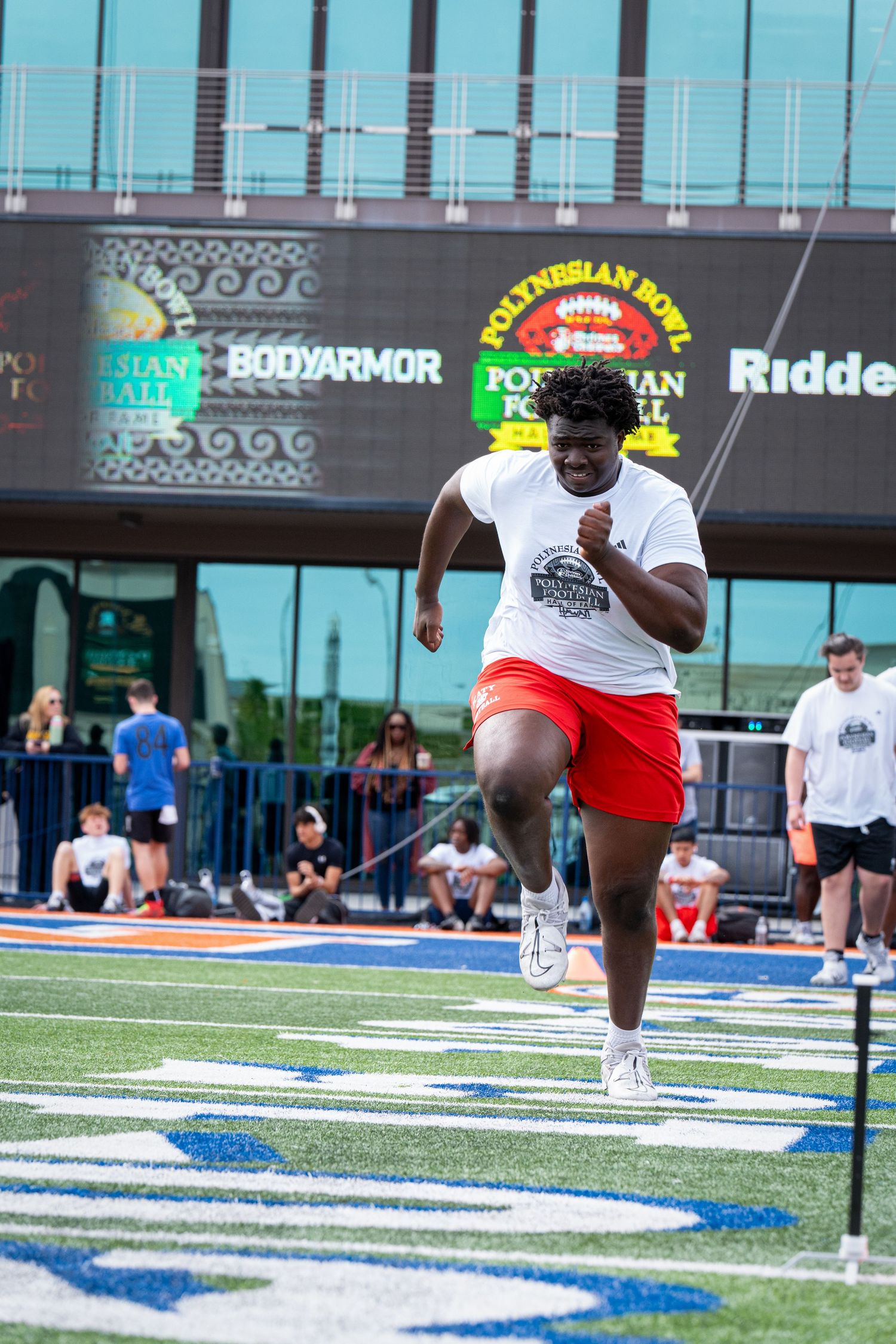 Player performs running drill on football field with stadium signage visible in background.