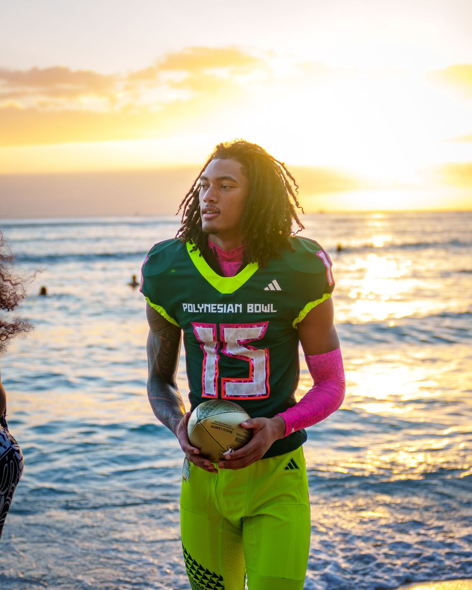 Football player in neon yellow uniform holds ball against dramatic beach sunset backdrop.