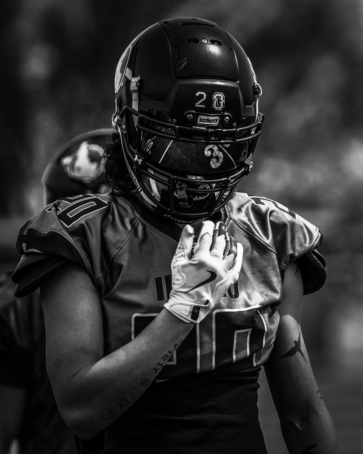 Football player in black uniform and helmet stands on field during night game.