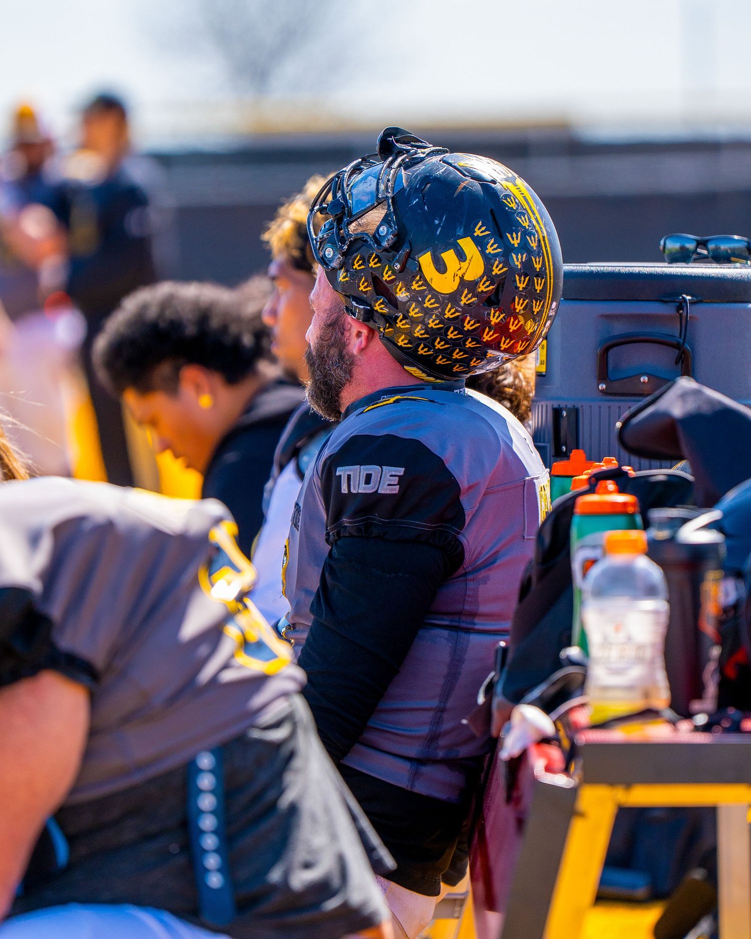 Football player wearing decorated navy helmet sits on sideline during game.
