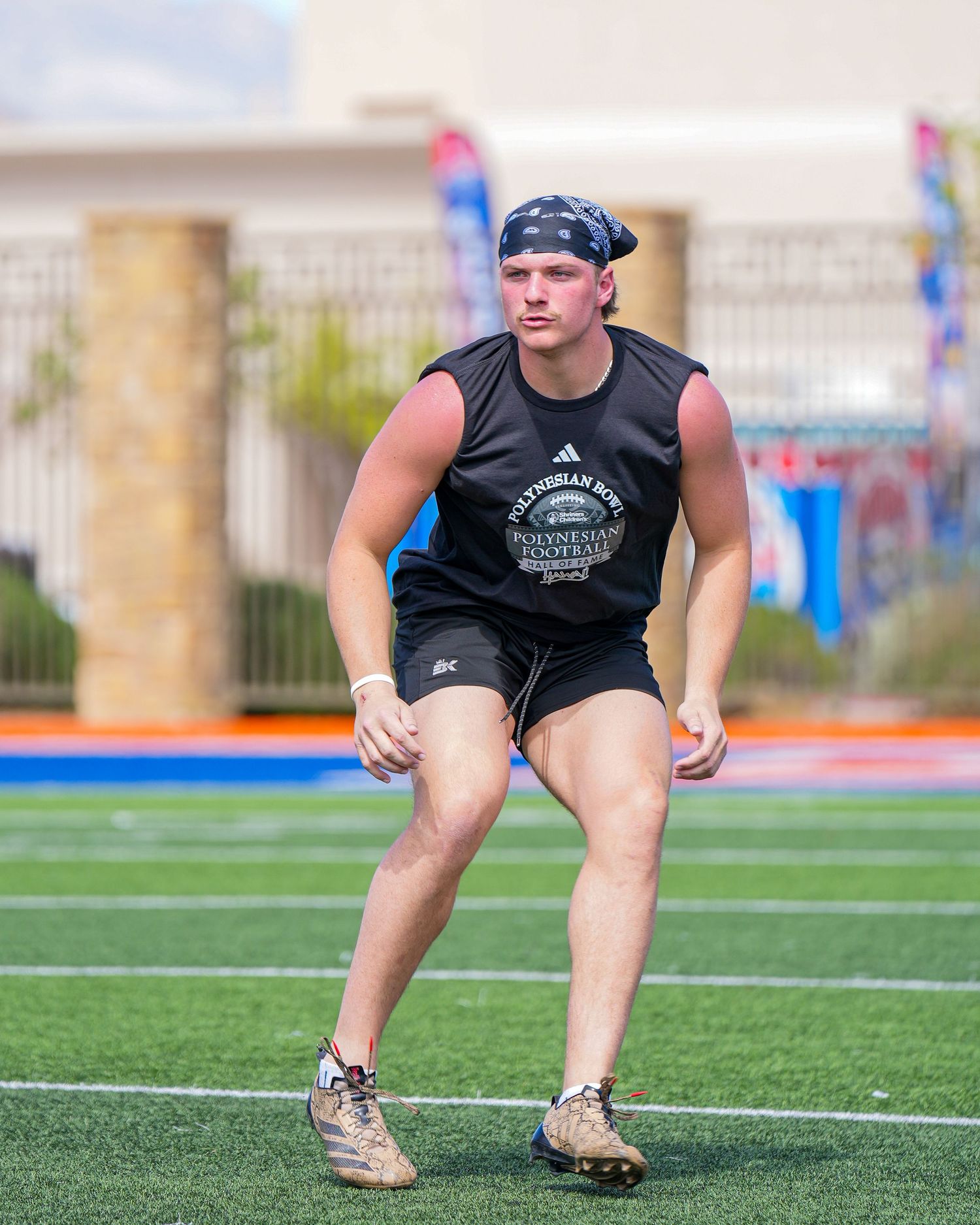 Athletic figure in black workout gear performs a dynamic stretching exercise on a turf field.