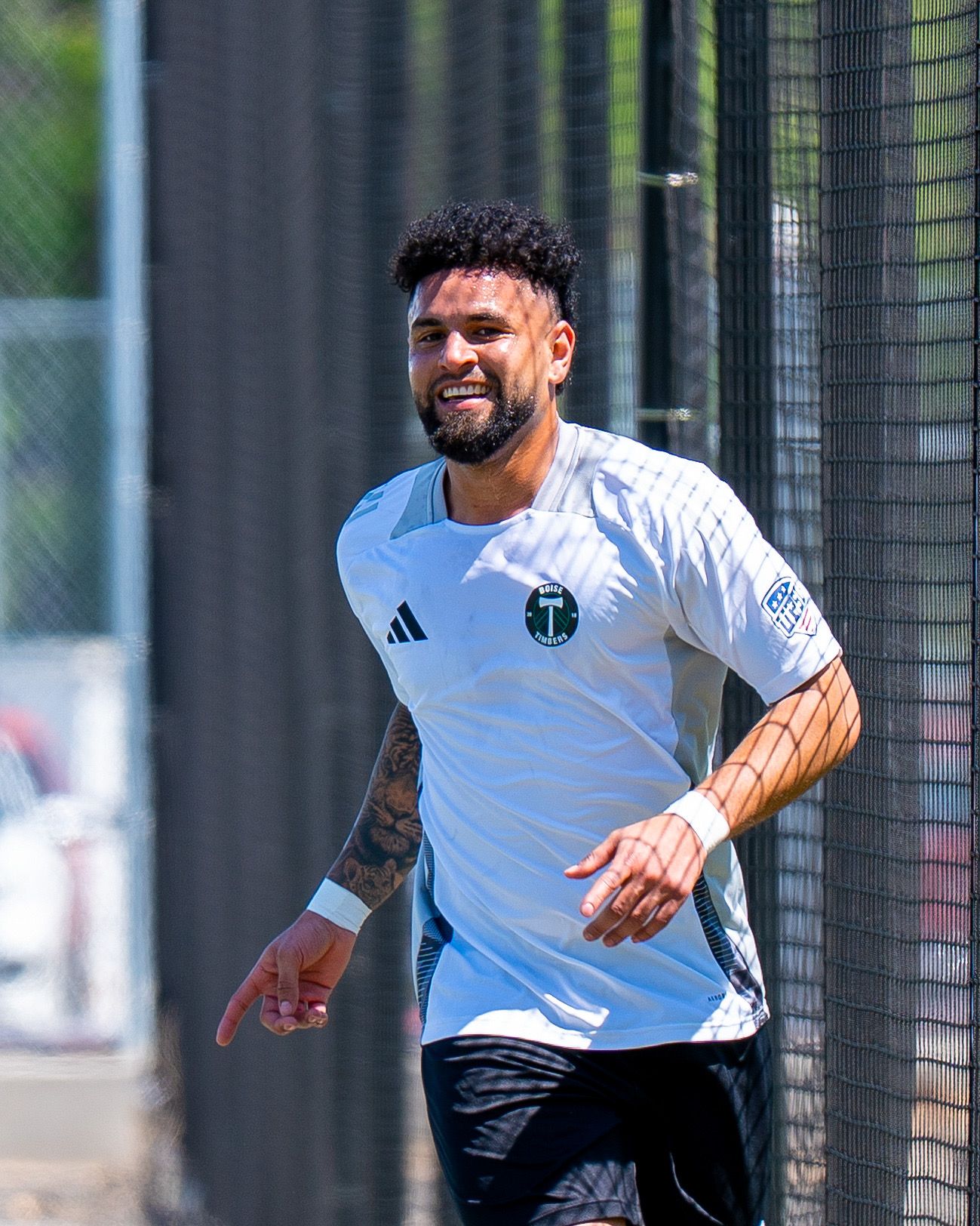 A soccer player wearing a white Sporting KC jersey smiles while training on the practice field.