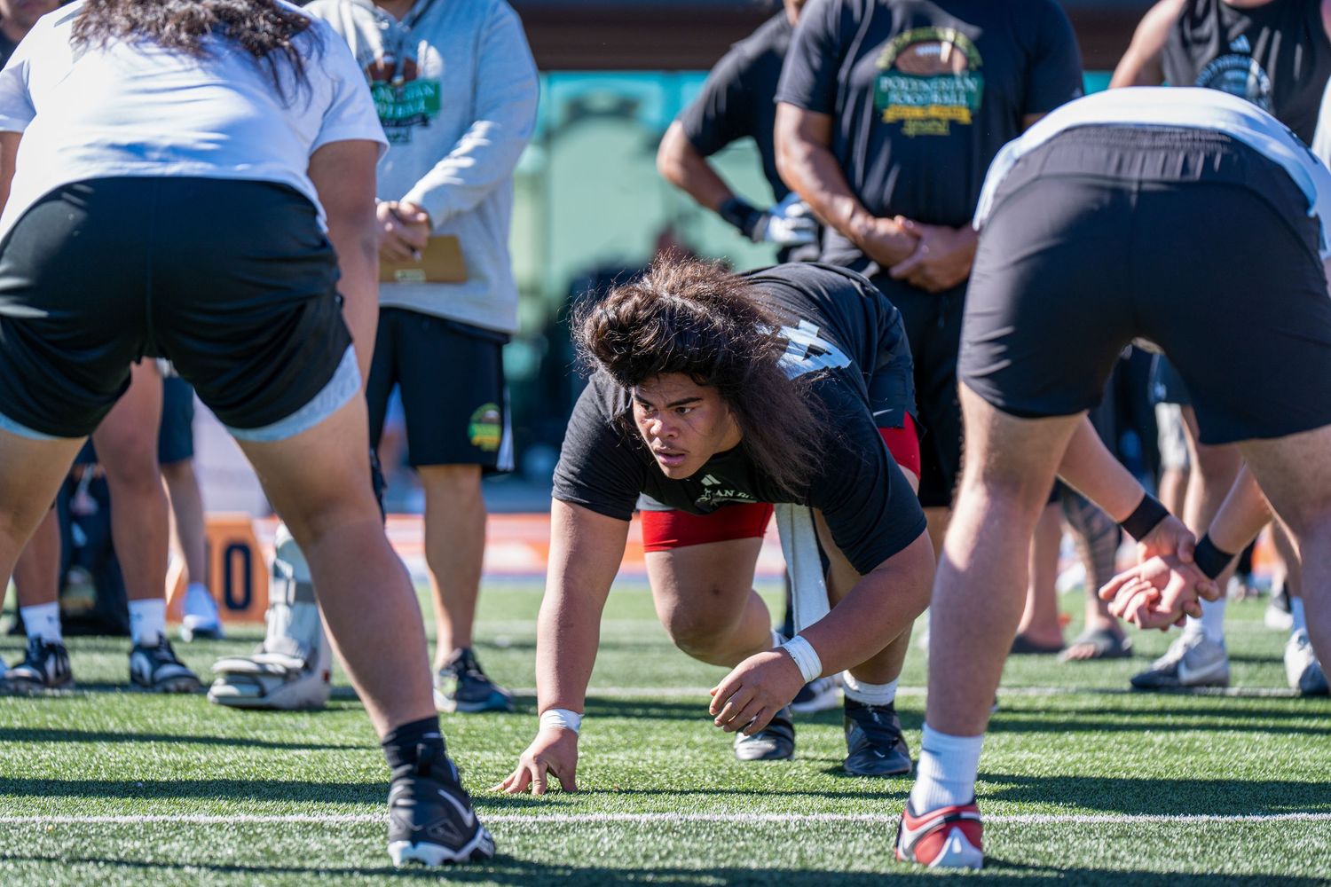 Athletes participate in group football training drill on artificial turf field.