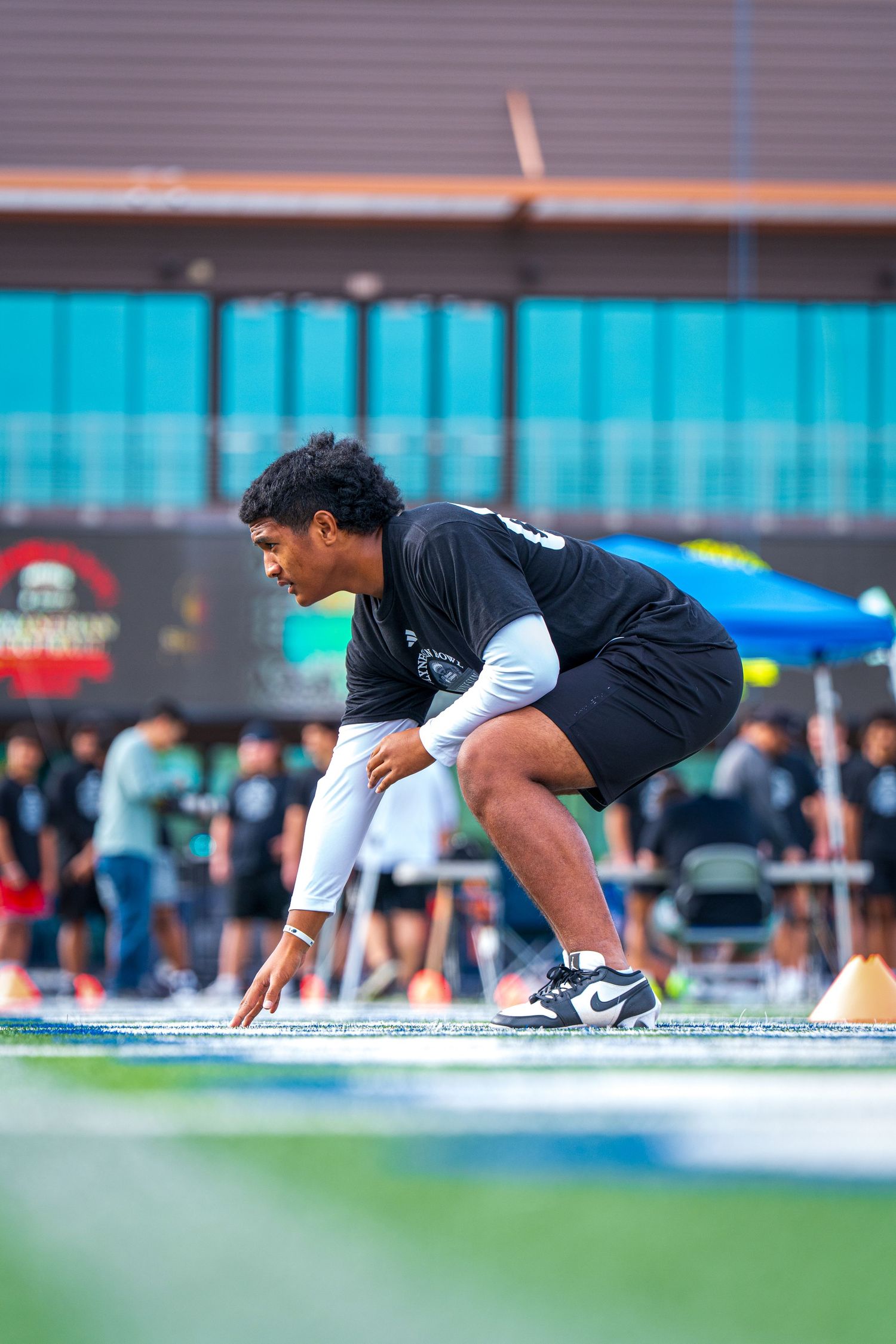 Athlete in dark training gear assumes sprinting stance on outdoor sports field.