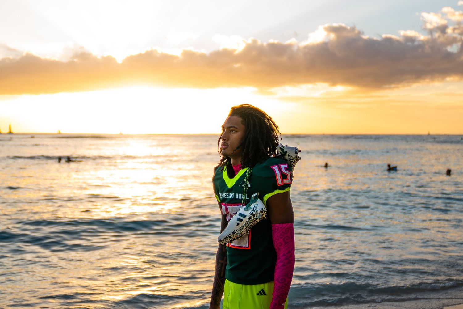 Silhouetted figure in neon wetsuit stands against golden ocean sunset with camera in hand.
