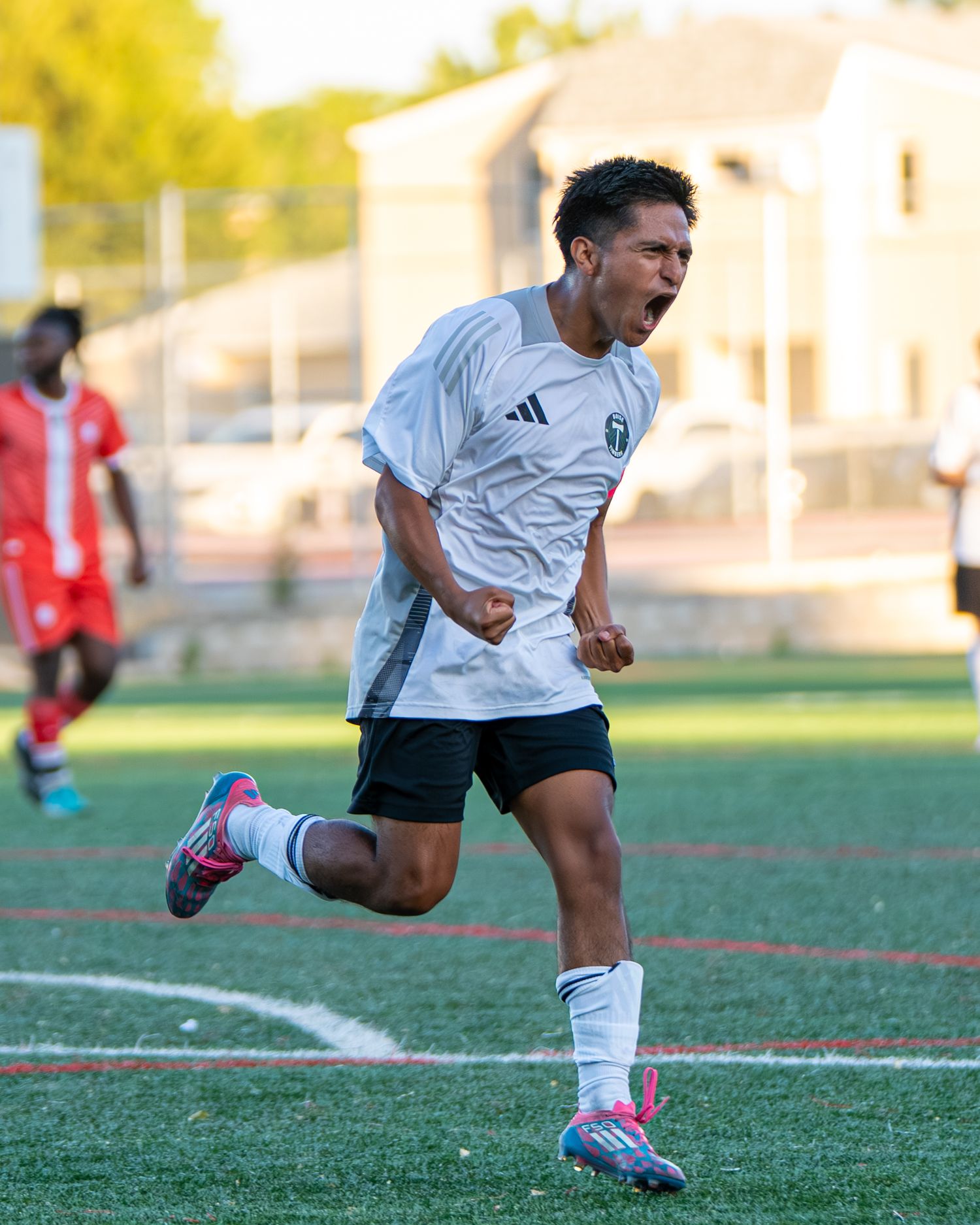 Soccer player in a white jersey and black shorts celebrates excitedly while running on an outdoor turf field.