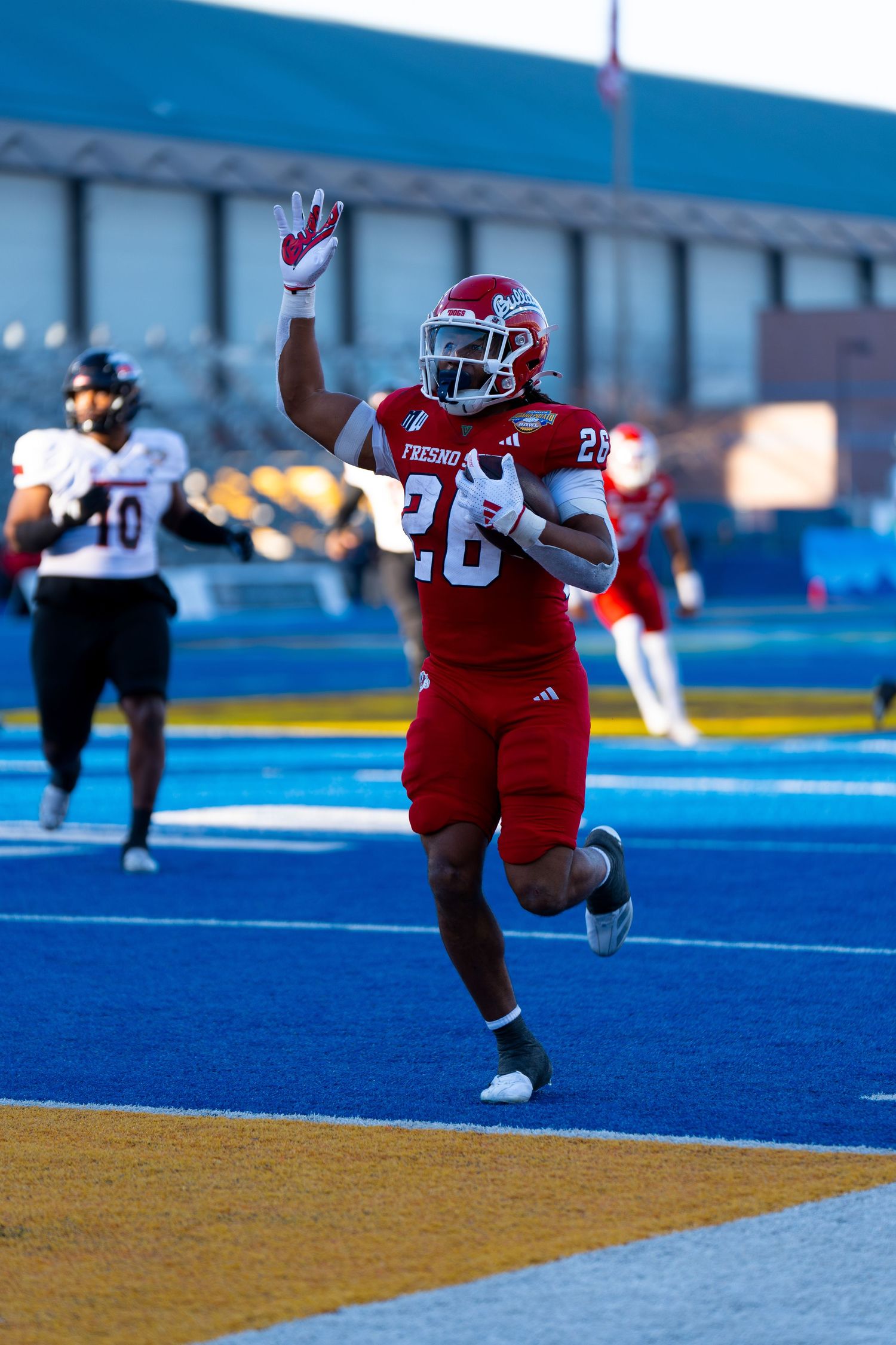 Football player in red uniform leaps to catch a pass on blue turf field during game action.