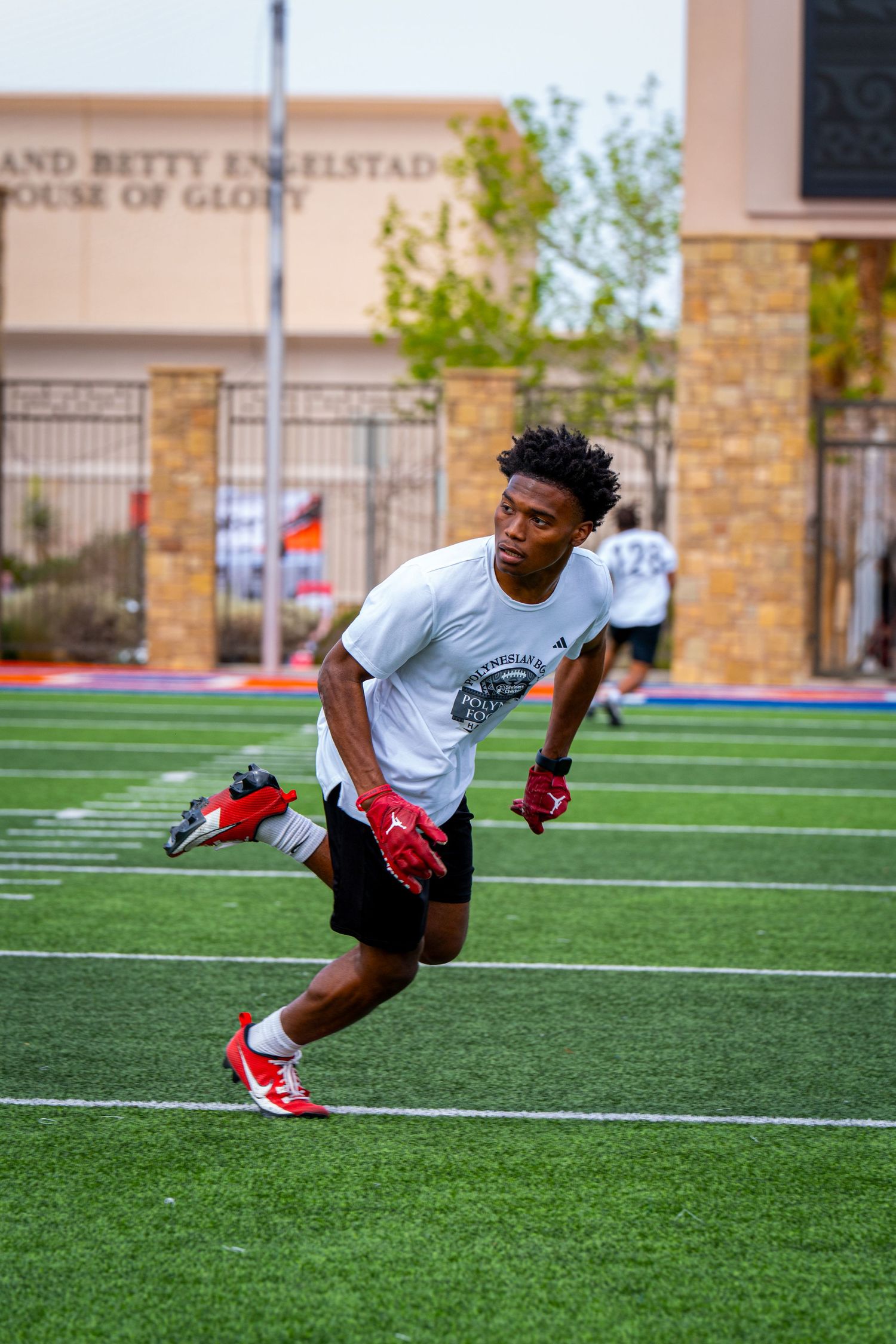 Player in white shirt and black shorts runs agility drill on football practice field.
