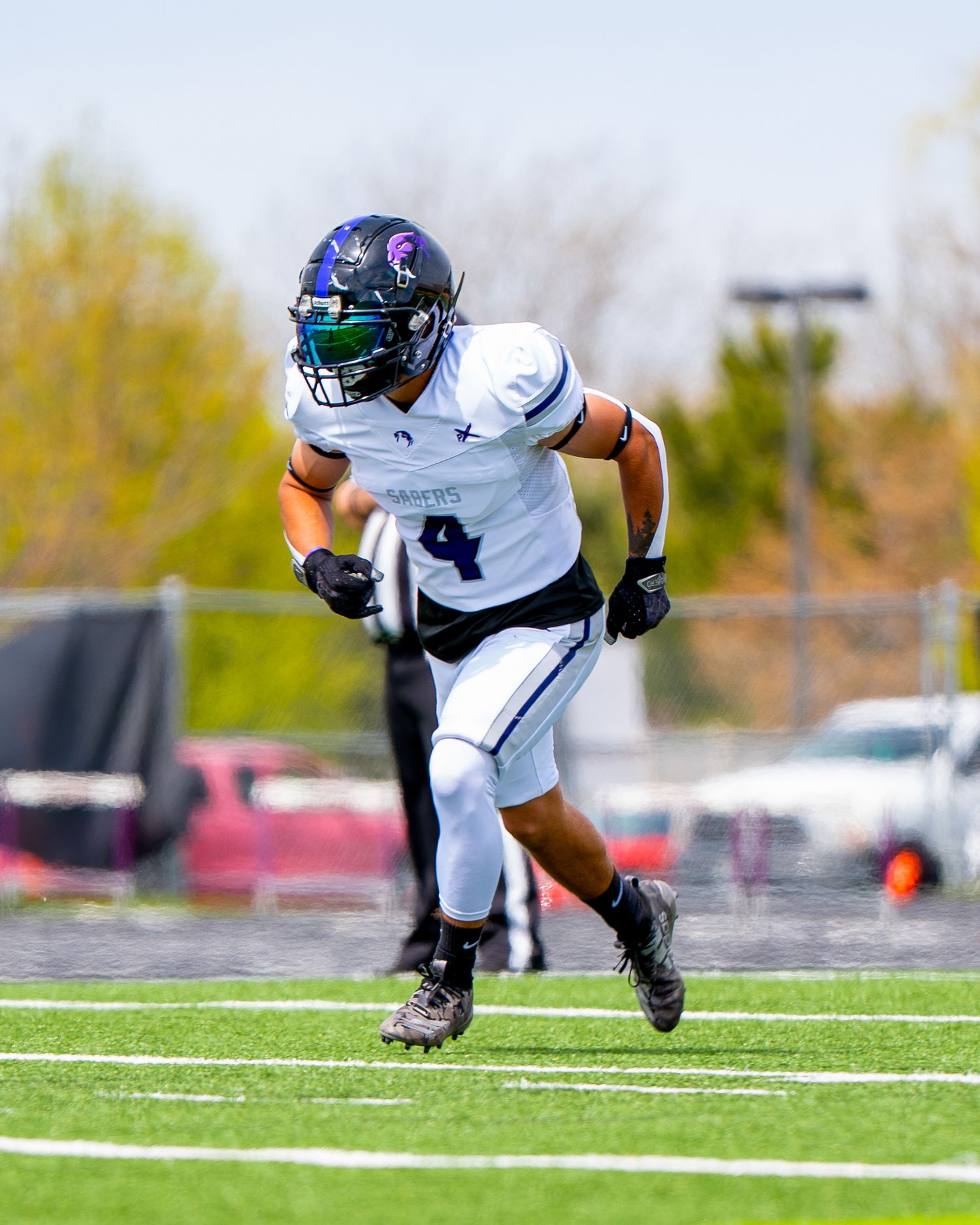 Running back in white uniform carries football while making cut on wet field.