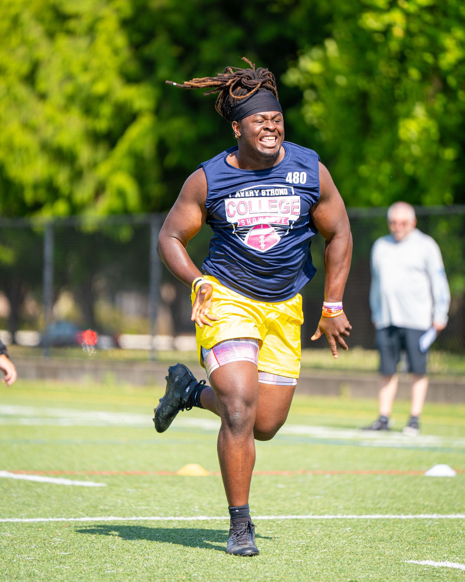 Athlete wearing number 480 sprints on a green turf field during a college football combine event on a sunny day.