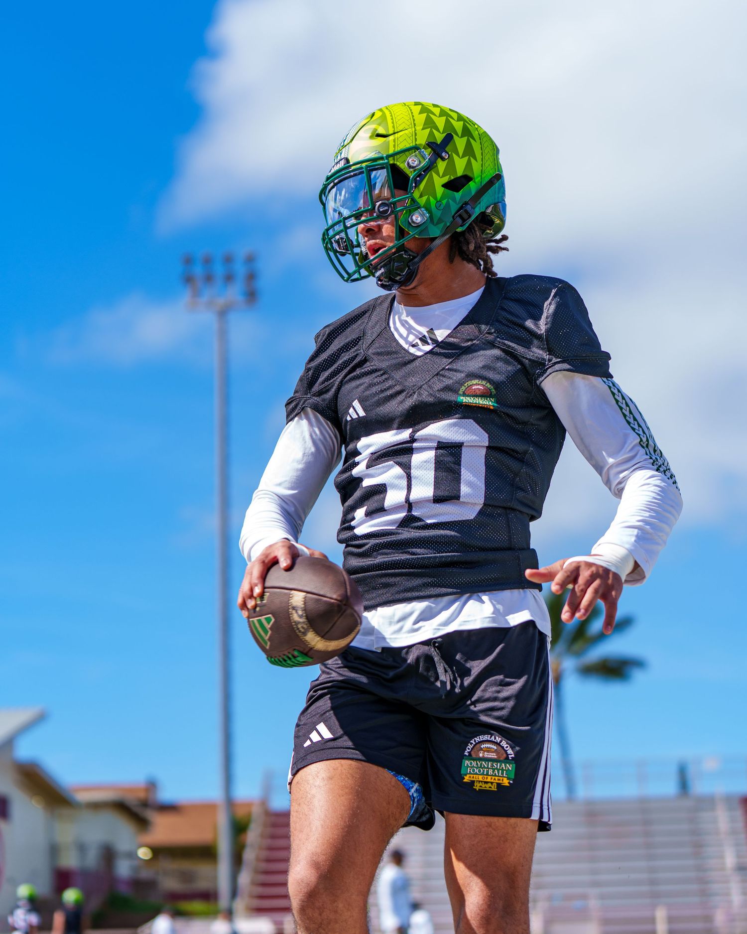 Football player in black jersey and white sleeves practices drills on sunny field during training session.