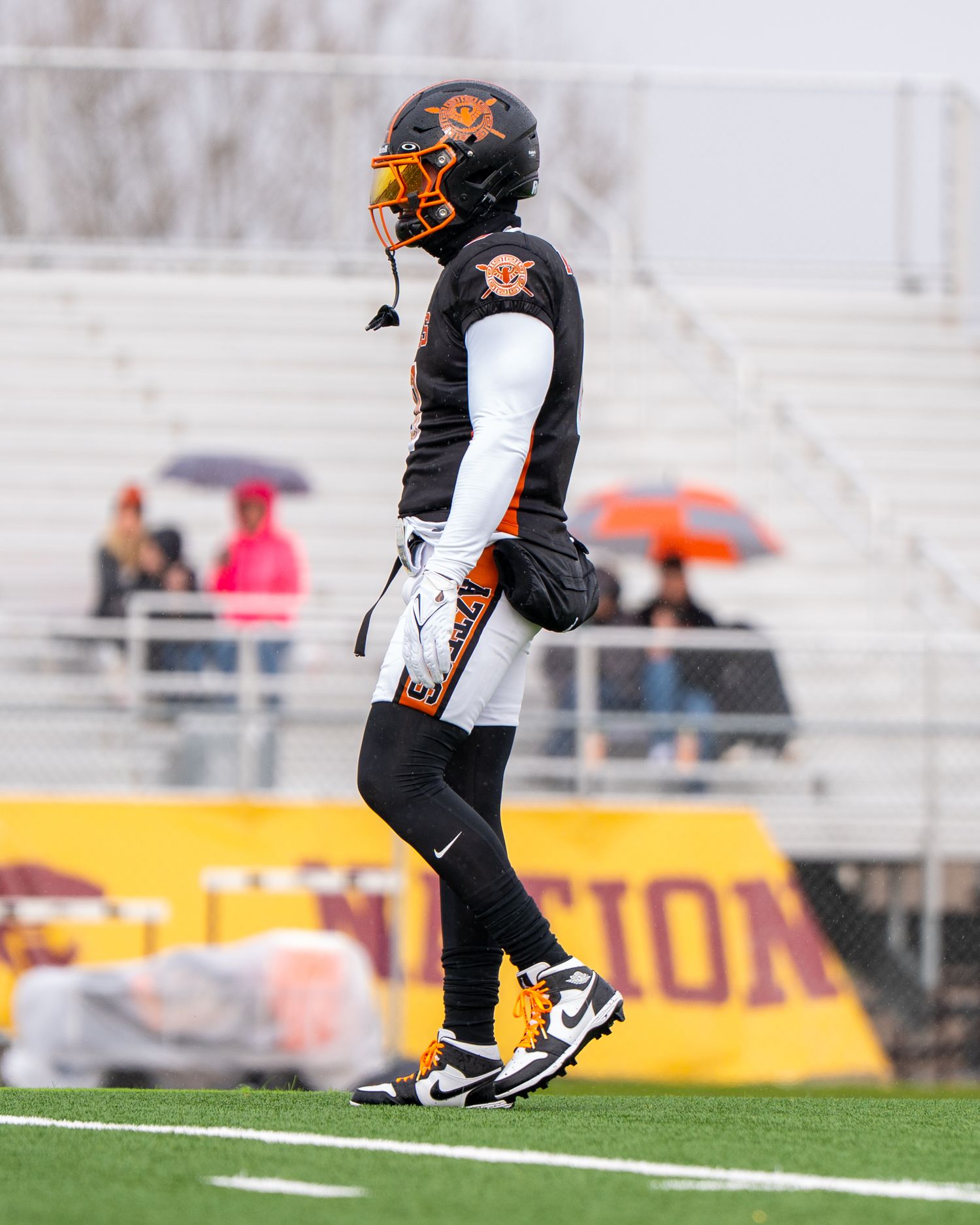 Player in black and orange uniform stands ready on football field during game.