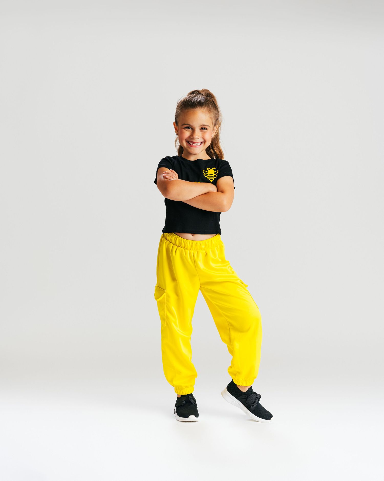 Young dancer in black top and yellow pants confidently posing with arms crossed in studio by Bylitos Studio Michigan
