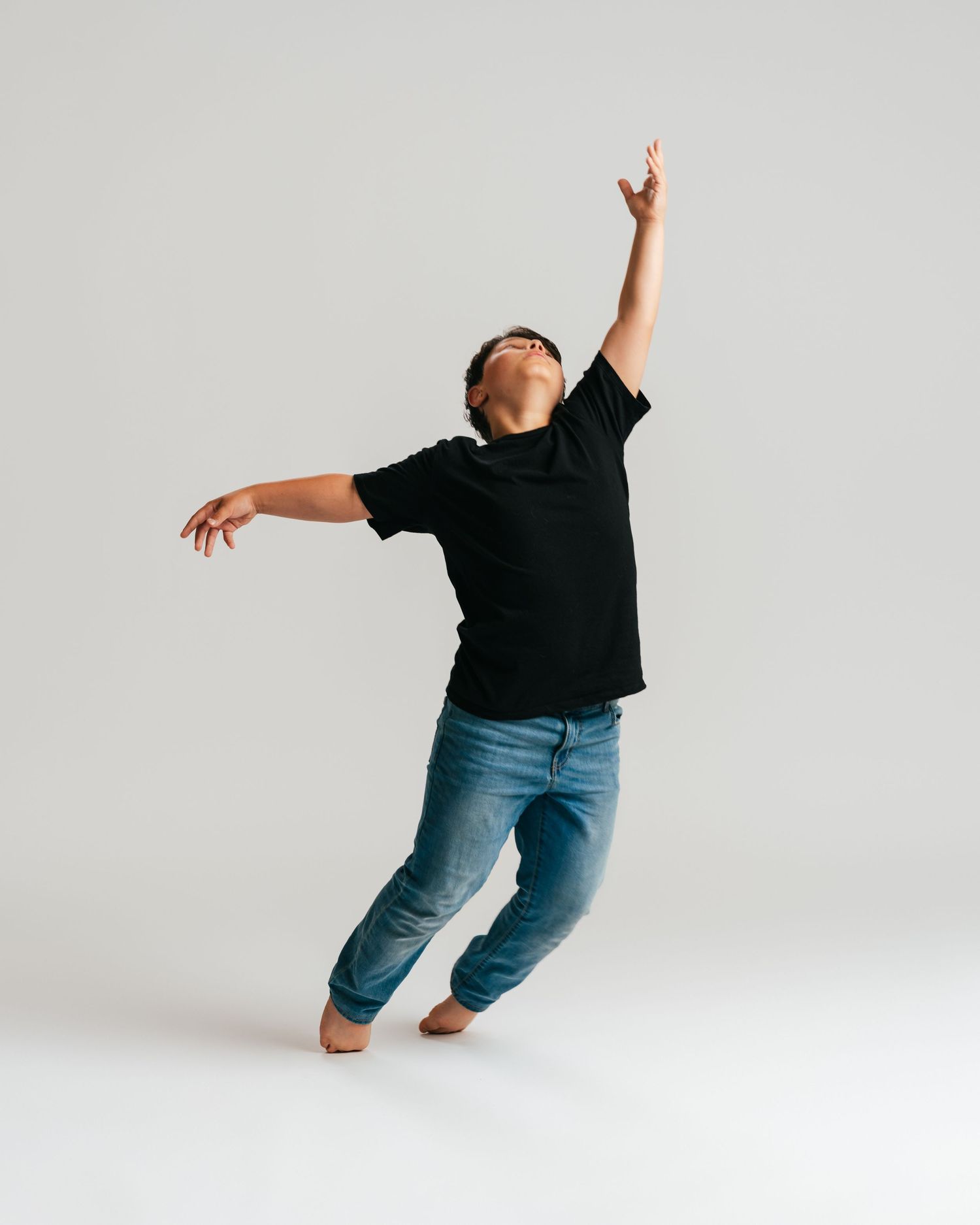 Male dancer in black tee and jeans reaching arms upward in studio editorial by Bylitos Studio Michigan