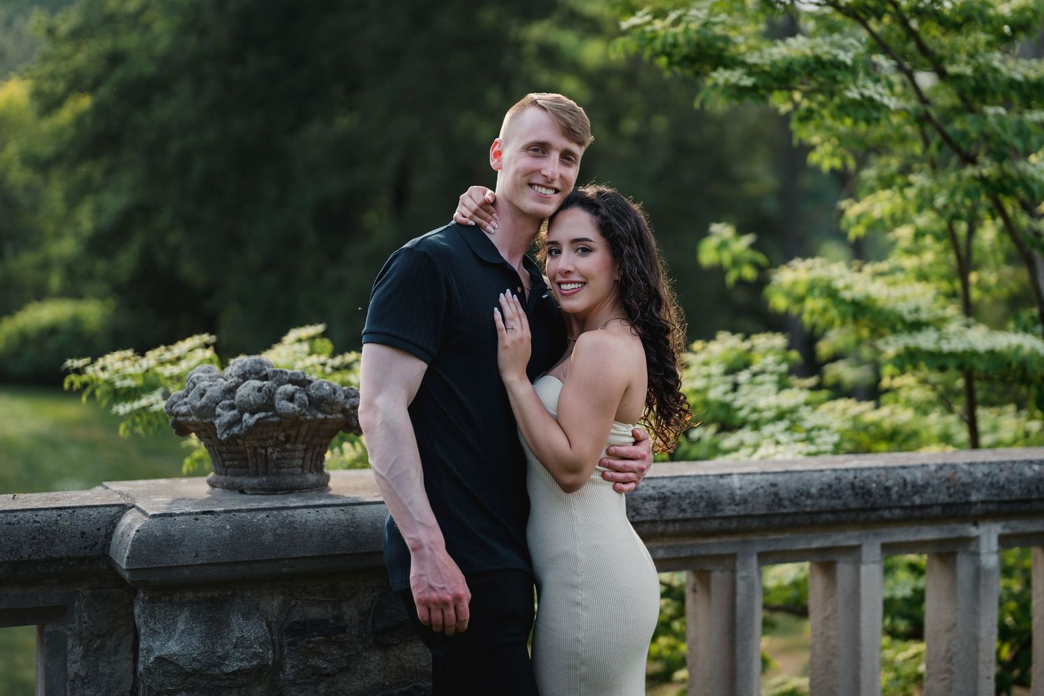 Engaged couple embracing at a stone terrace surrounded by lush greenery by Bylitos Studio Michigan