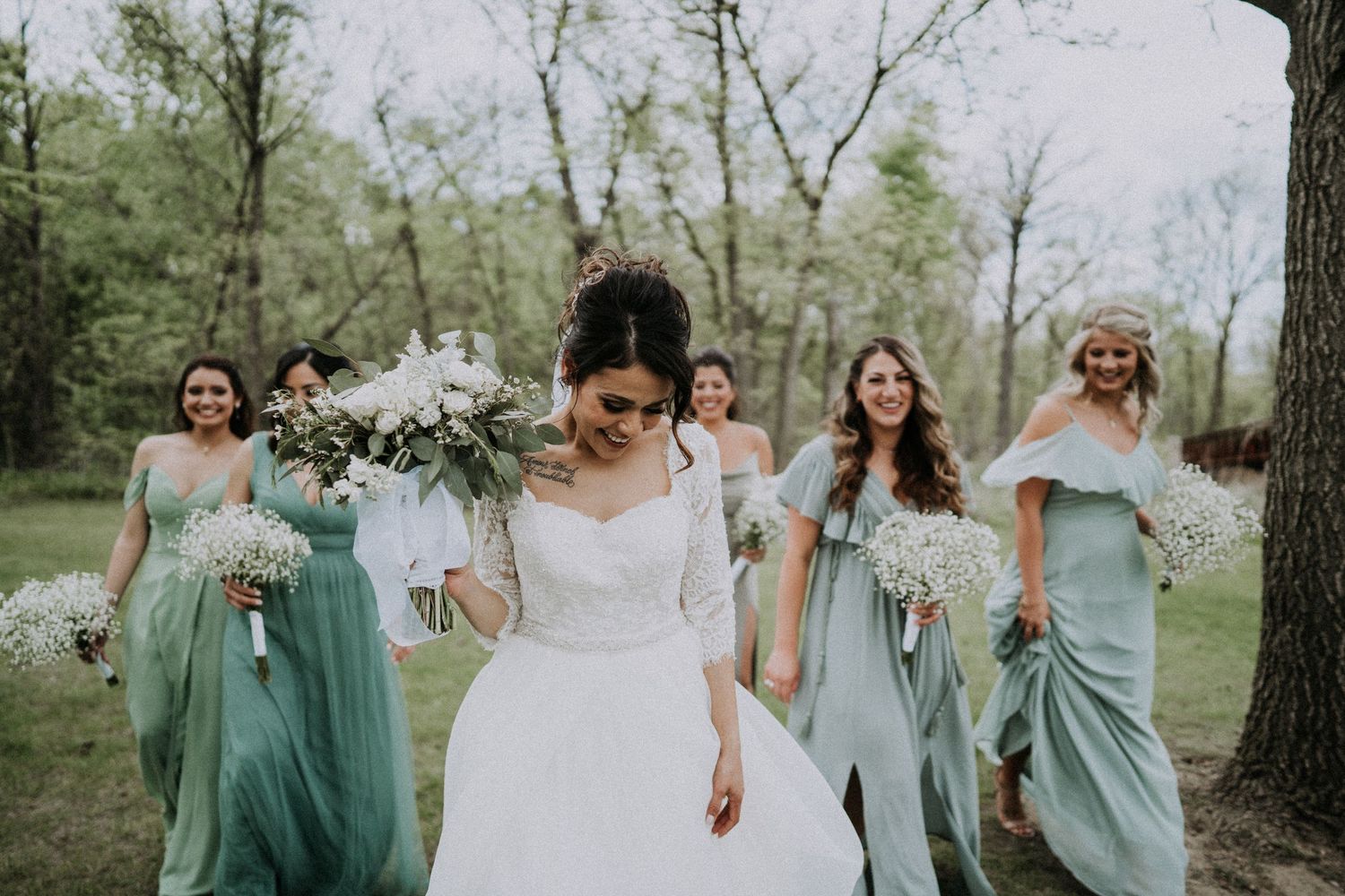 Bride leading bridesmaids in sage dresses through a wooded outdoor setting by Bylitos Studio Michigan