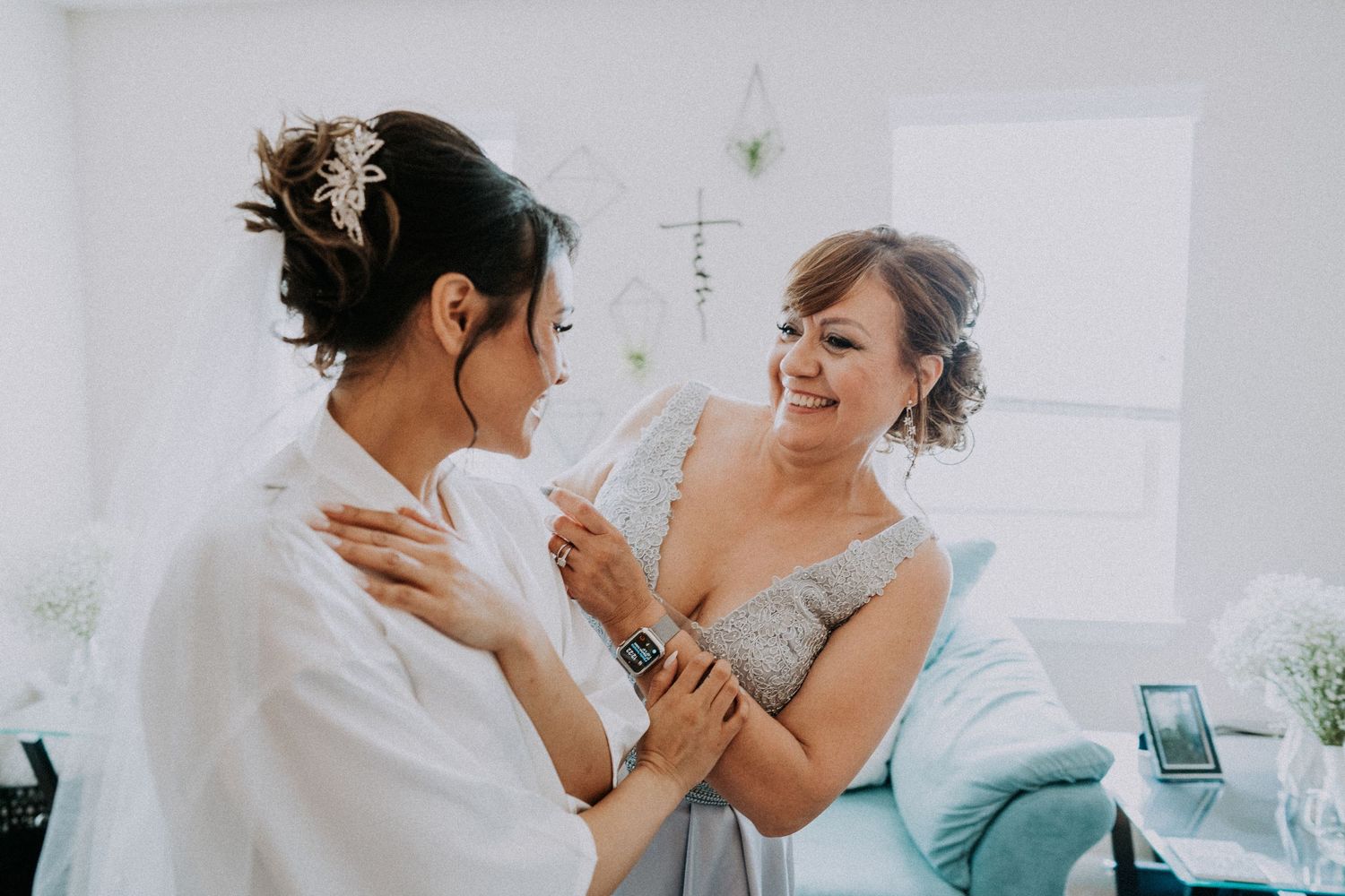 Bride smiling as bridesmaid helps her prepare on Michigan wedding day by Bylitos Studio Michigan