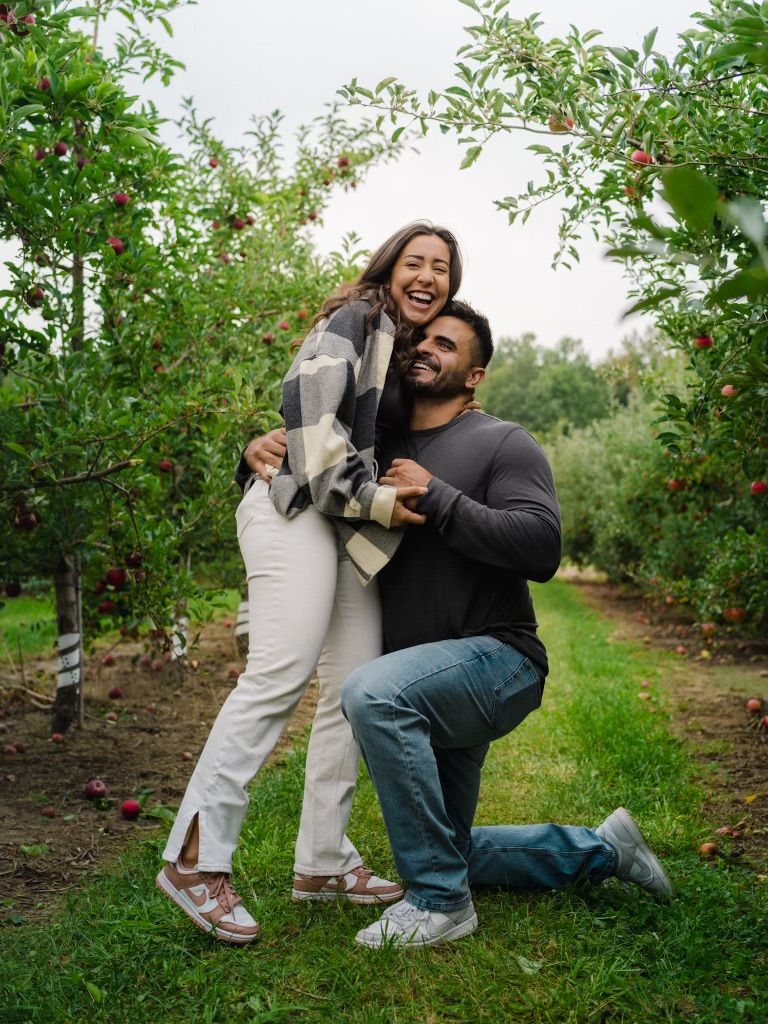 Playful engagement couple laughing in an orchard during fall lifestyle session by Bylitos Studio Michigan