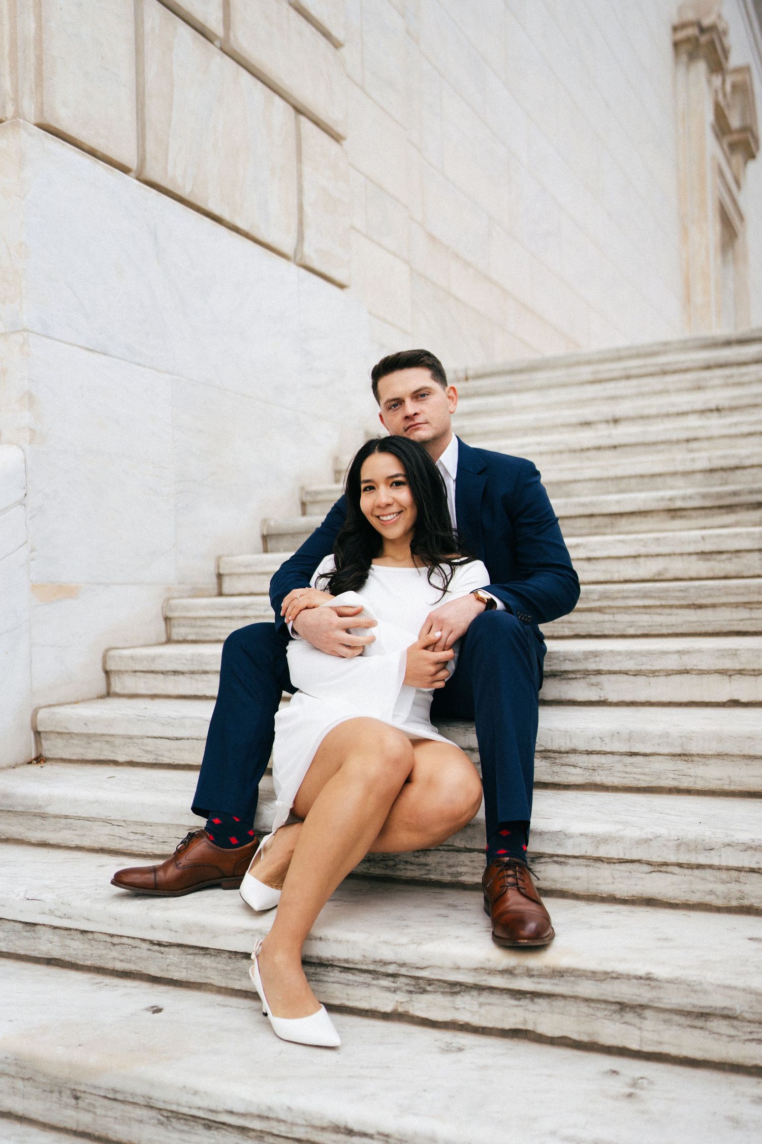Engaged couple seated together on marble steps during Detroit engagement session by Bylitos Studio Michigan