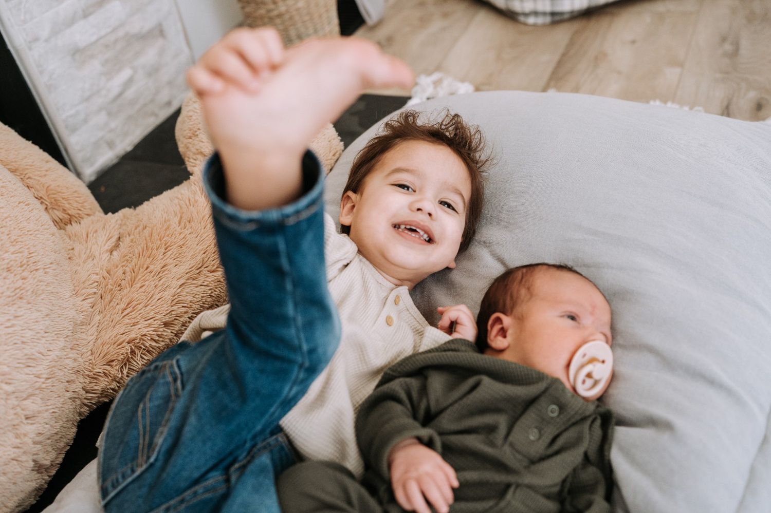 Joyful toddler waving next to newborn sibling in a sweet family lifestyle session by Bylitos Studio Michigan