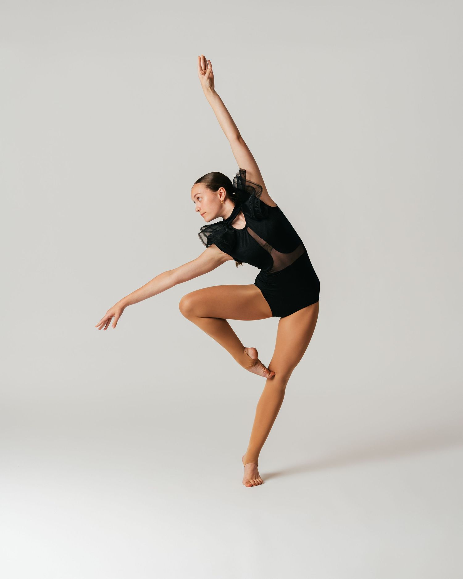 Dancer in black leotard mid-balance with arm raised high during studio editorial session by Bylitos Studio Michigan